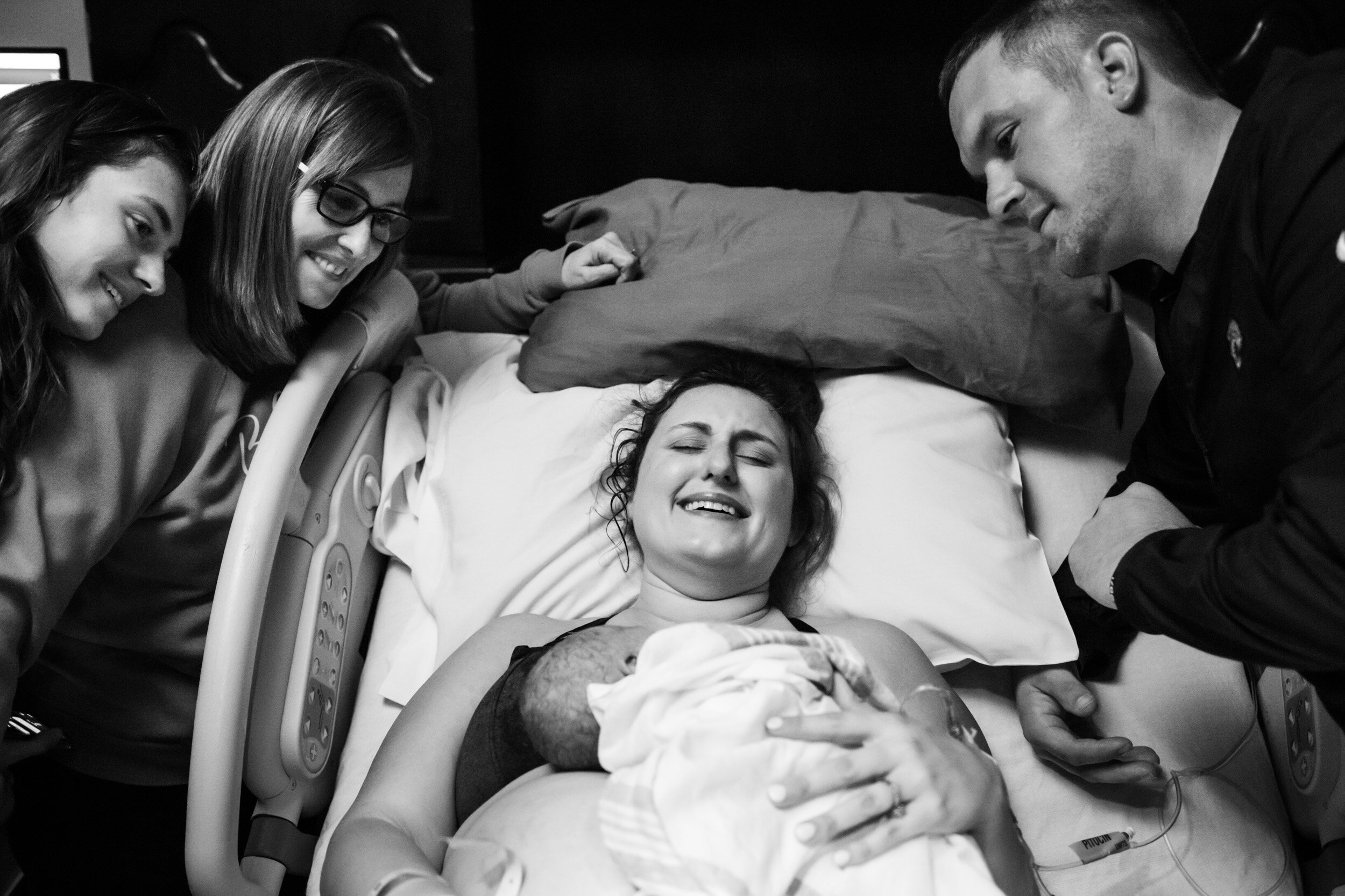 mom crying with joy while surrounded by family just after she birthed her baby