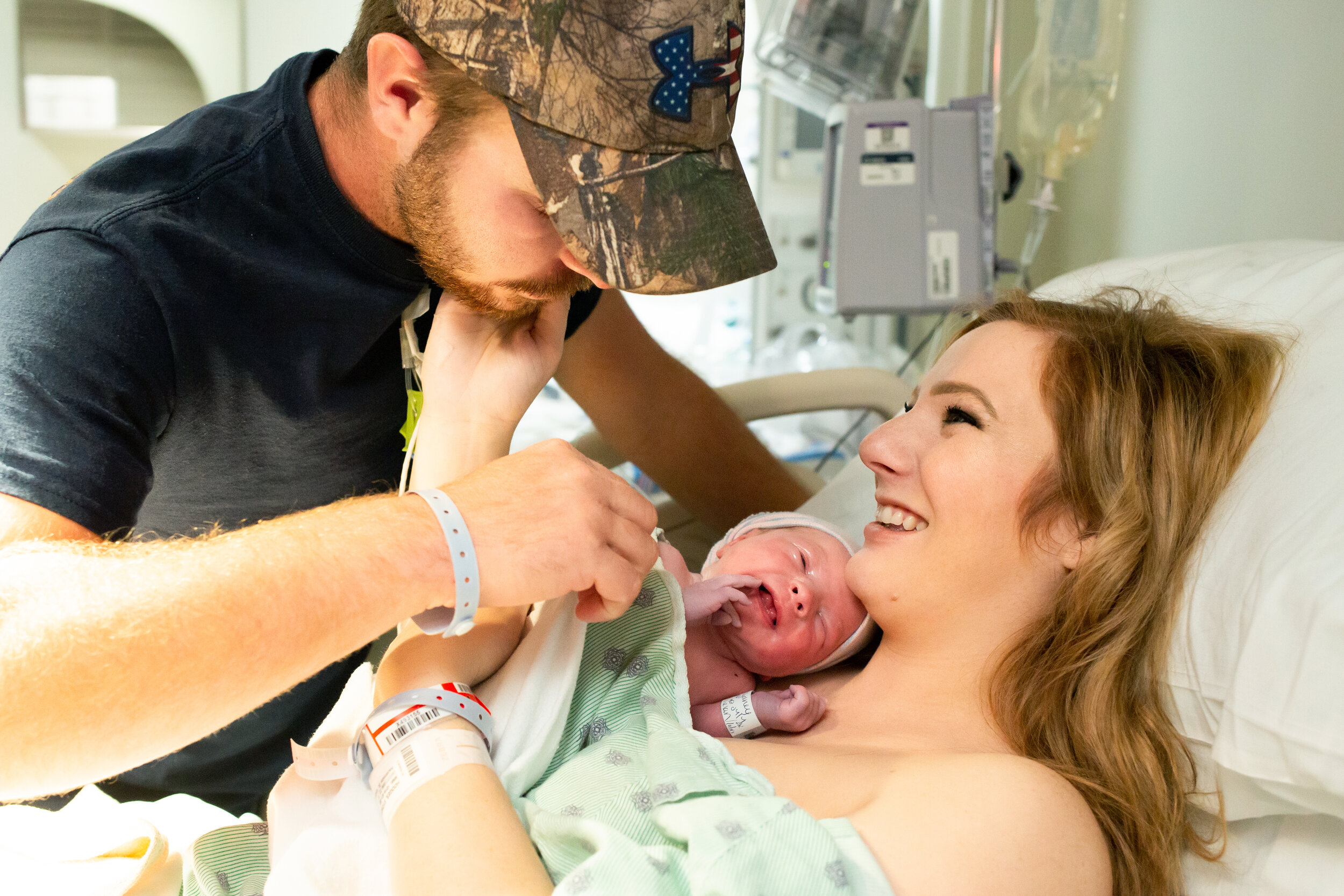 wife smiling at husband while he looks at their newborn baby