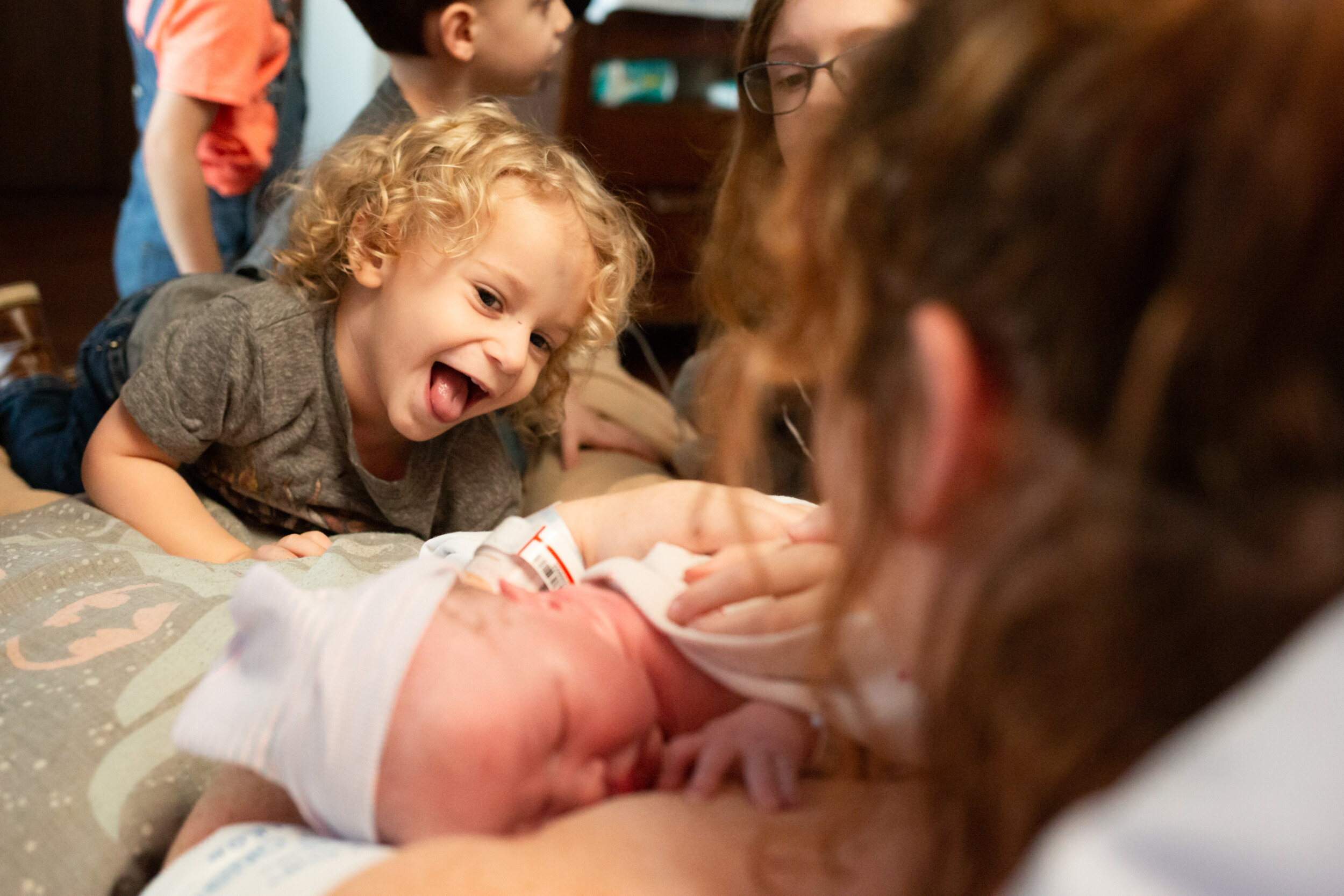 toddler sticking tongue out and laughing at newborn baby brother