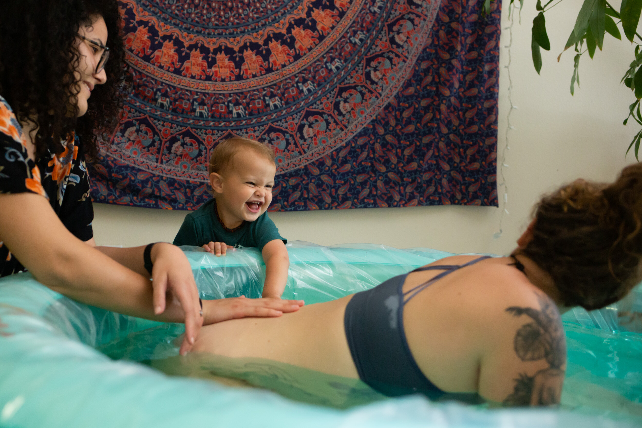 little boy and midwife looking at mom while she labors in birth pool