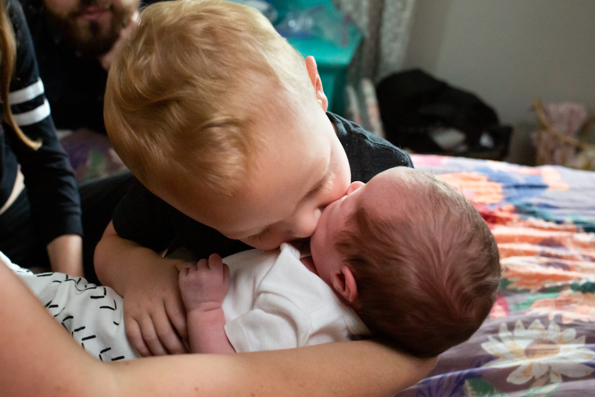 big brother kissing newborn baby sister