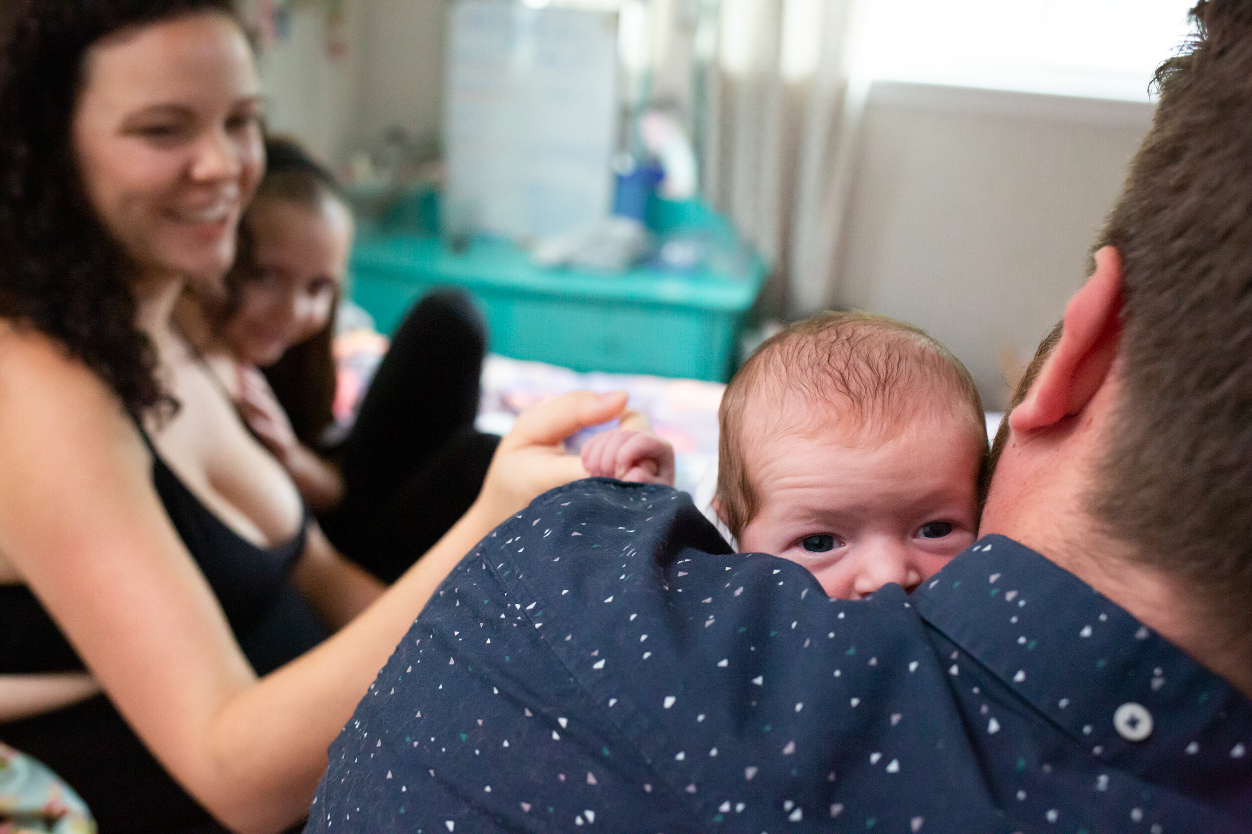 dad holding newborn baby girl while mother holds her hand