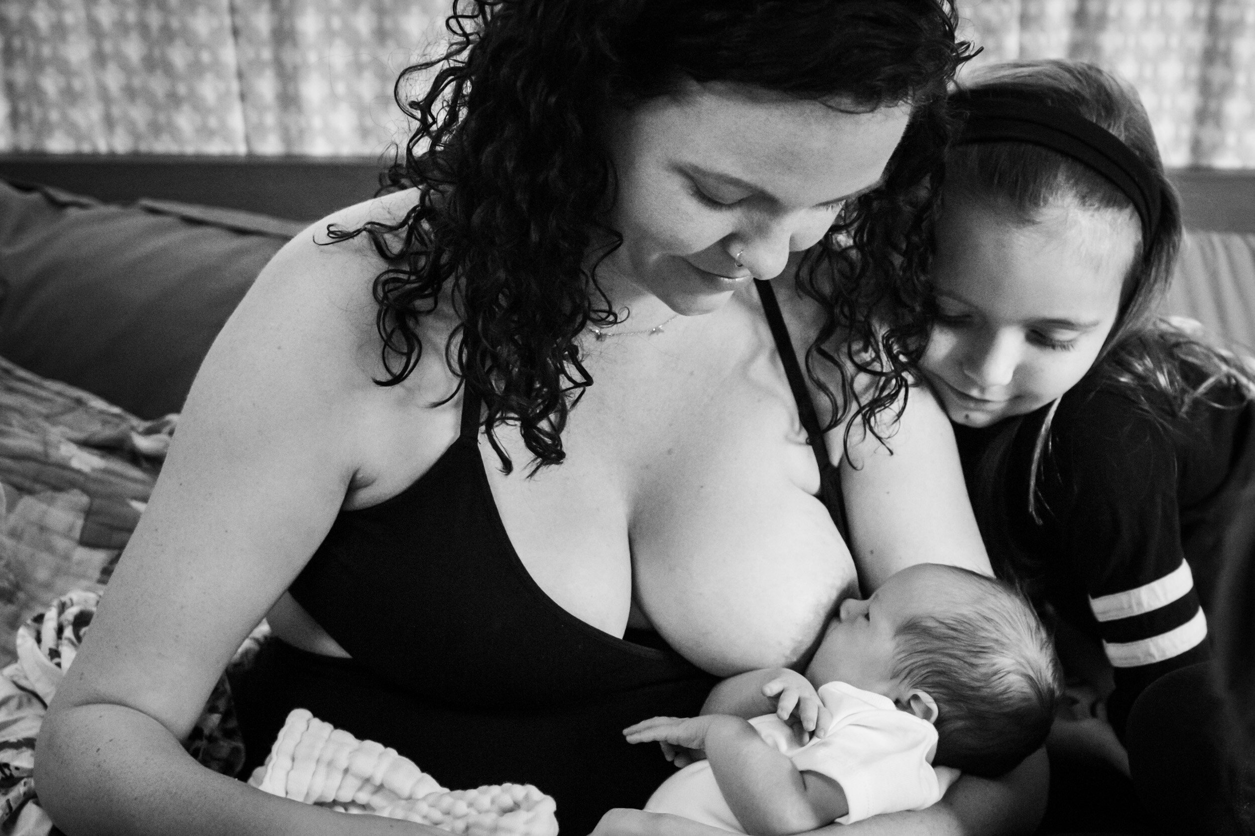 oldest daughter admiring baby sister as mom breastfeeds