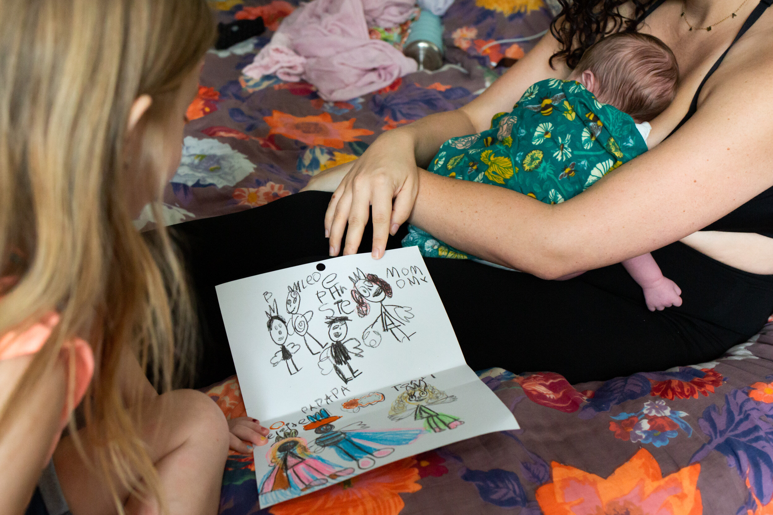 little girl presenting drawing of the family to mom with newborn baby sister