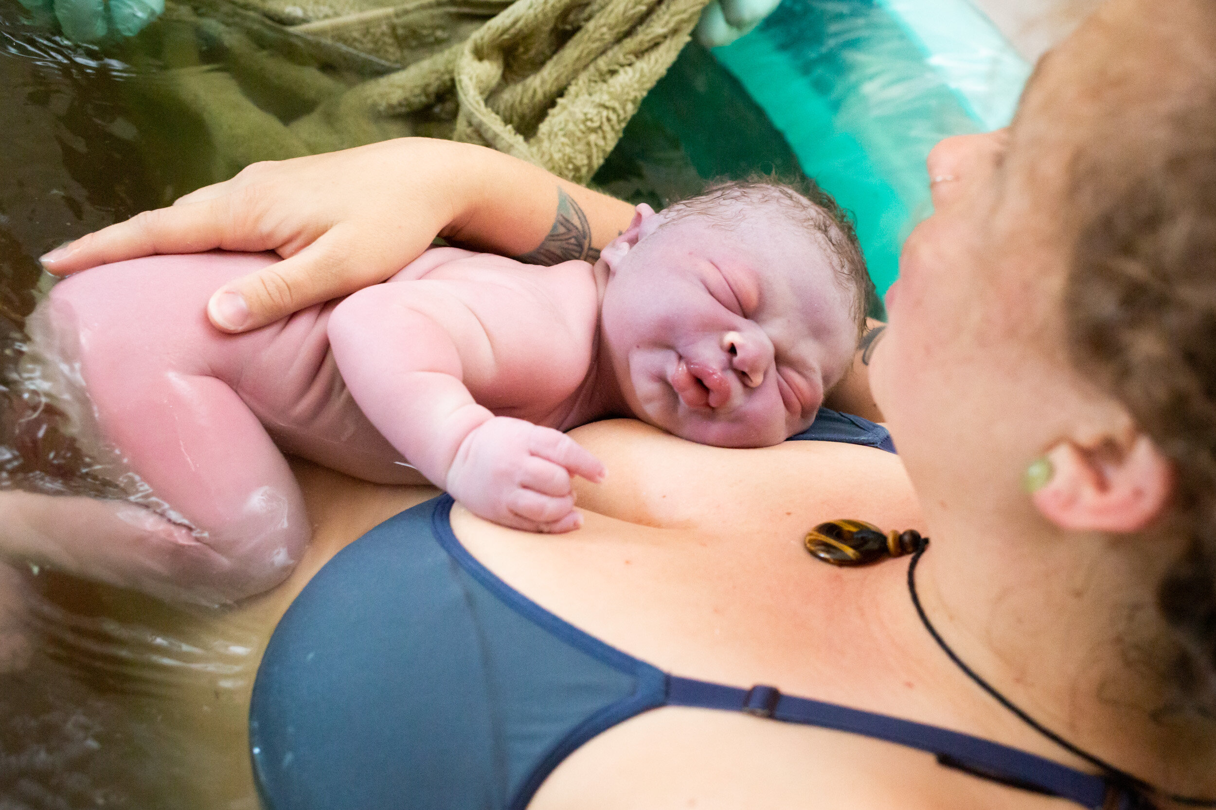 newborn baby resting on mother in birth pool