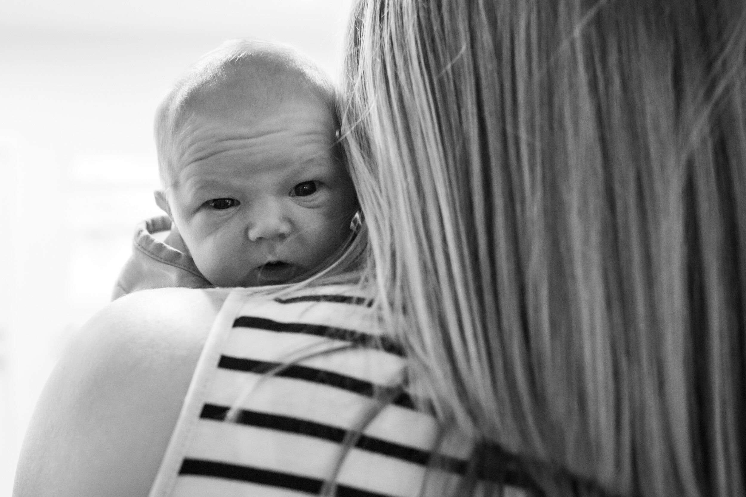 newborn baby boy peeking over mom's shoulder