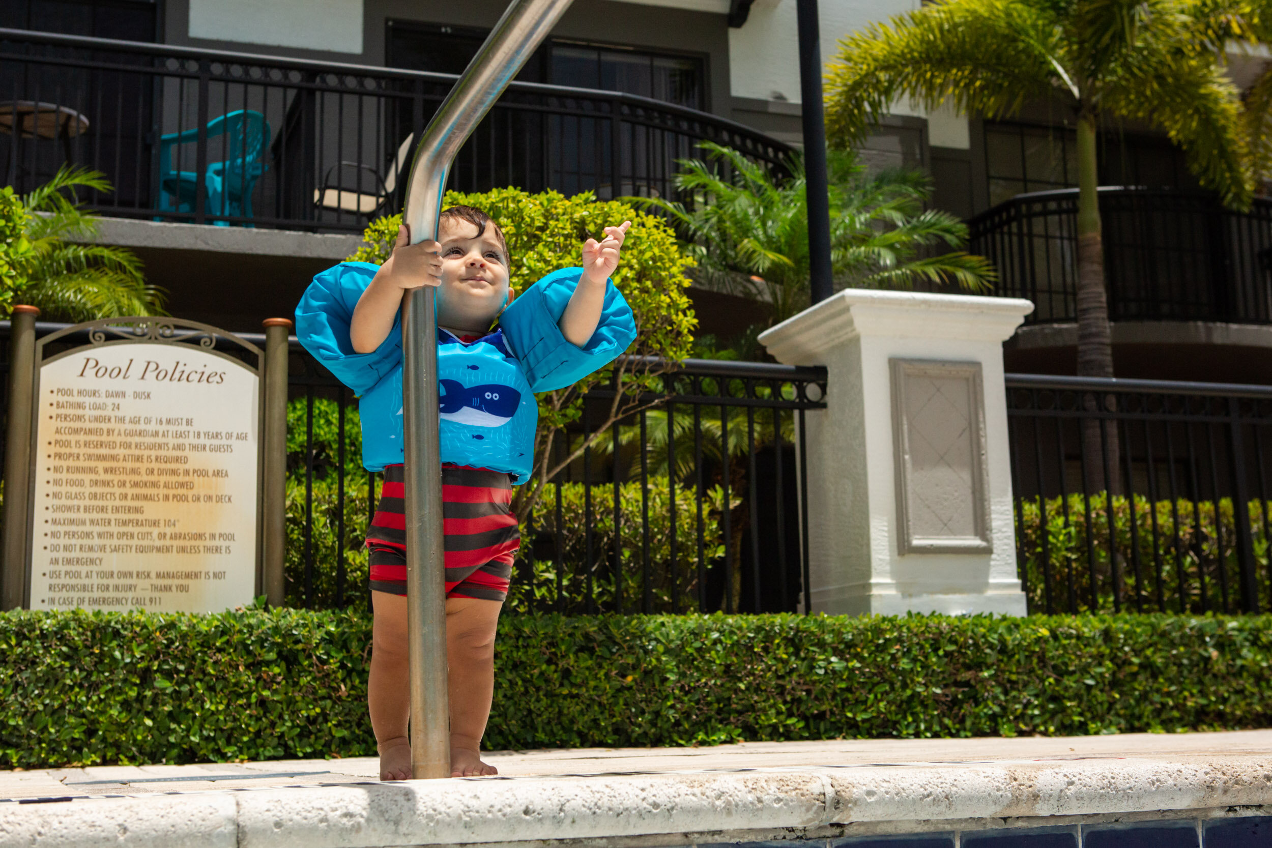 little boy reaching up to the pool railing