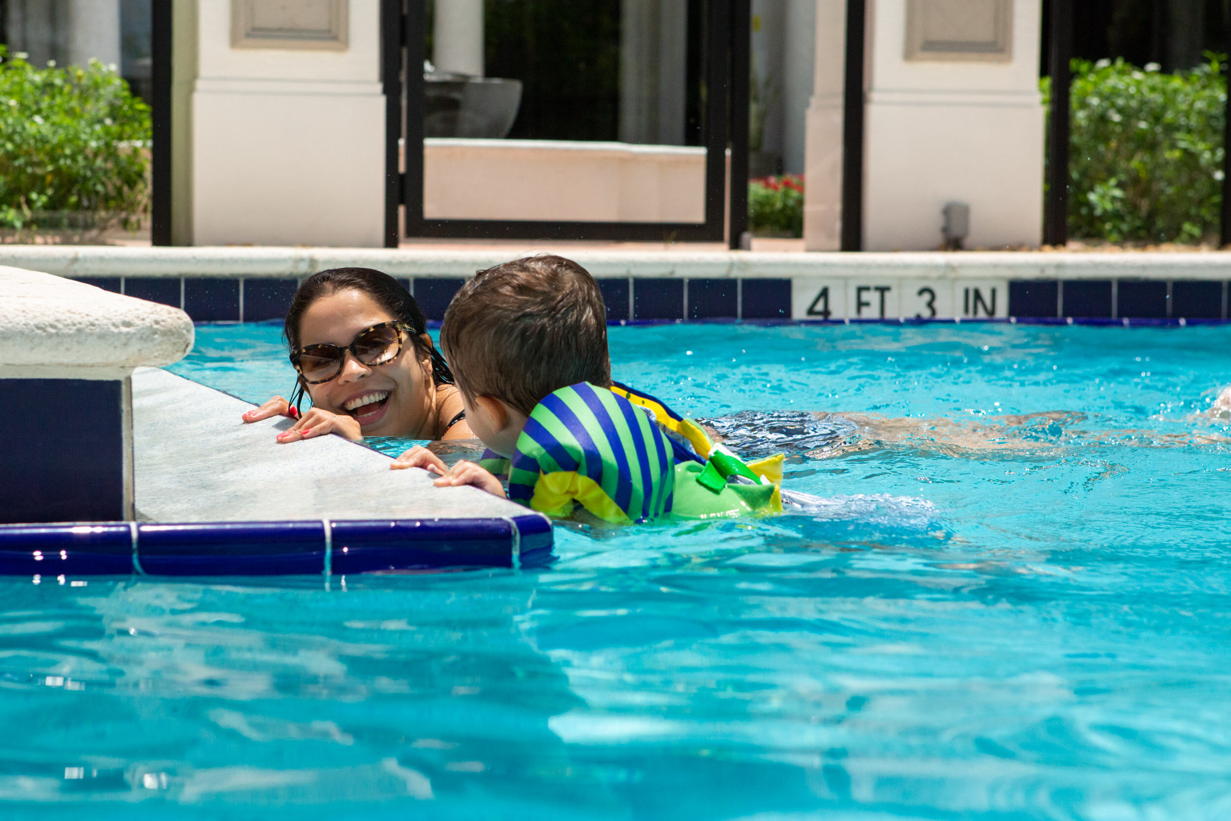 mom smiling at little boy while kicking in the pool