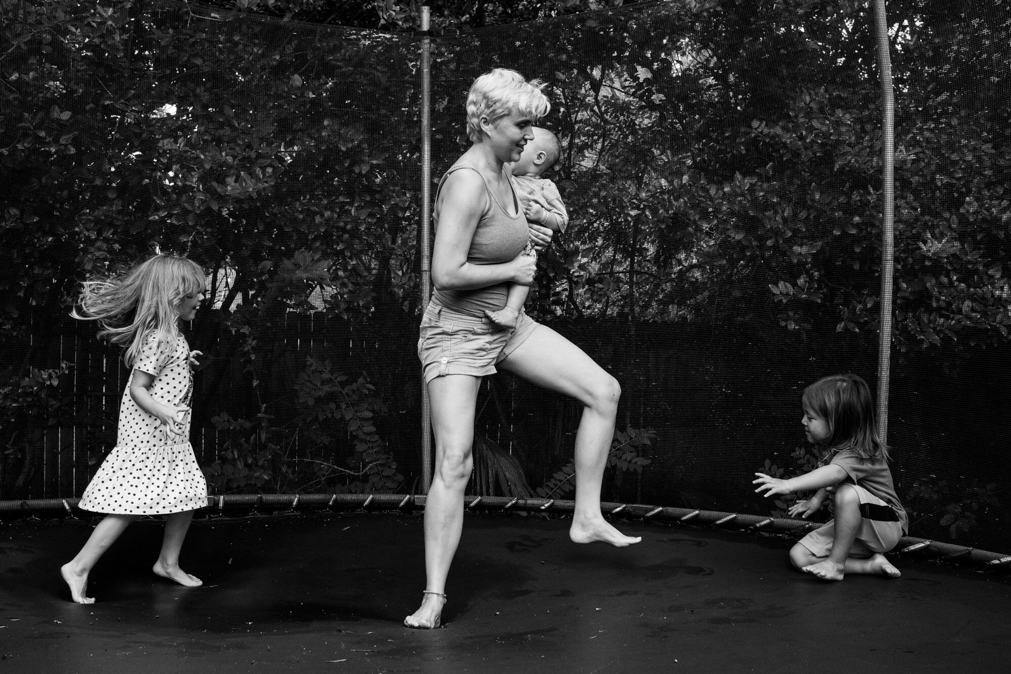 mom holding baby while playing on trampoline with older children