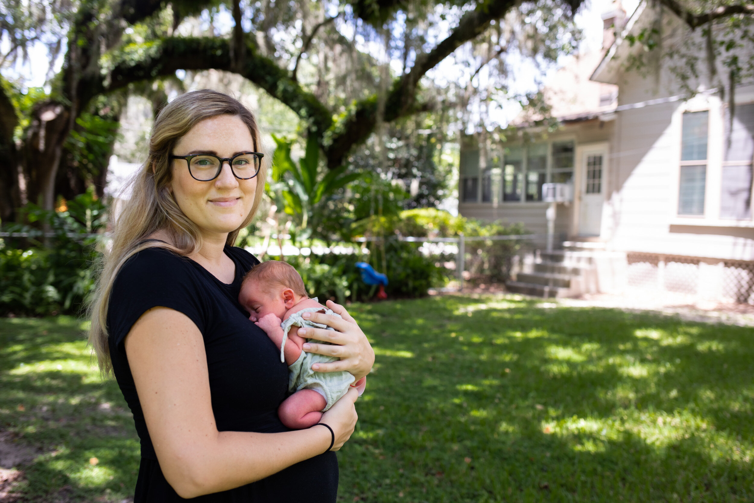 new mom smiling and holding her baby outside their home