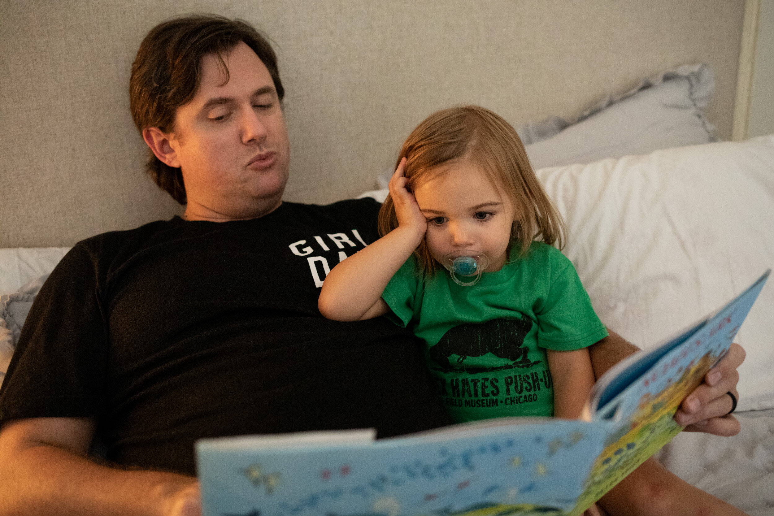 little girl reading with her dad while leaning on him