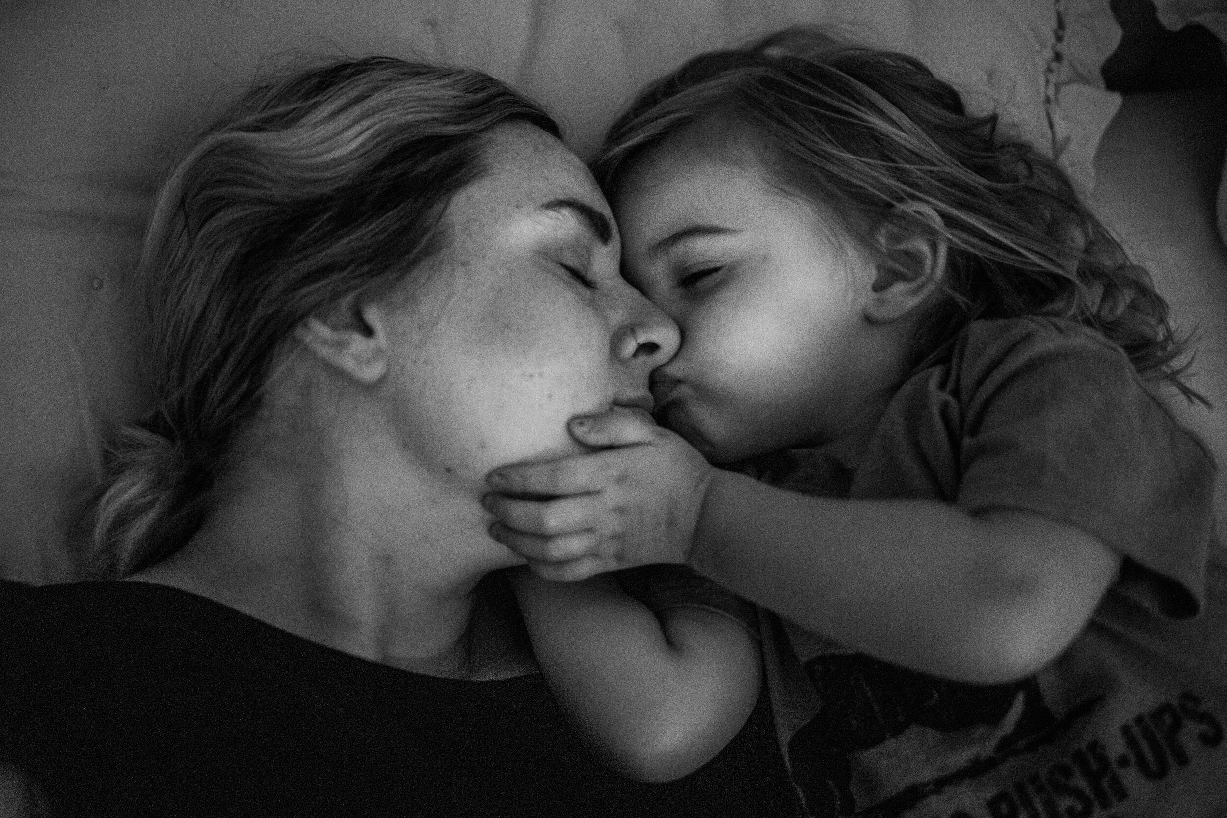 little girl holding her mom's face and kissing her goodnight