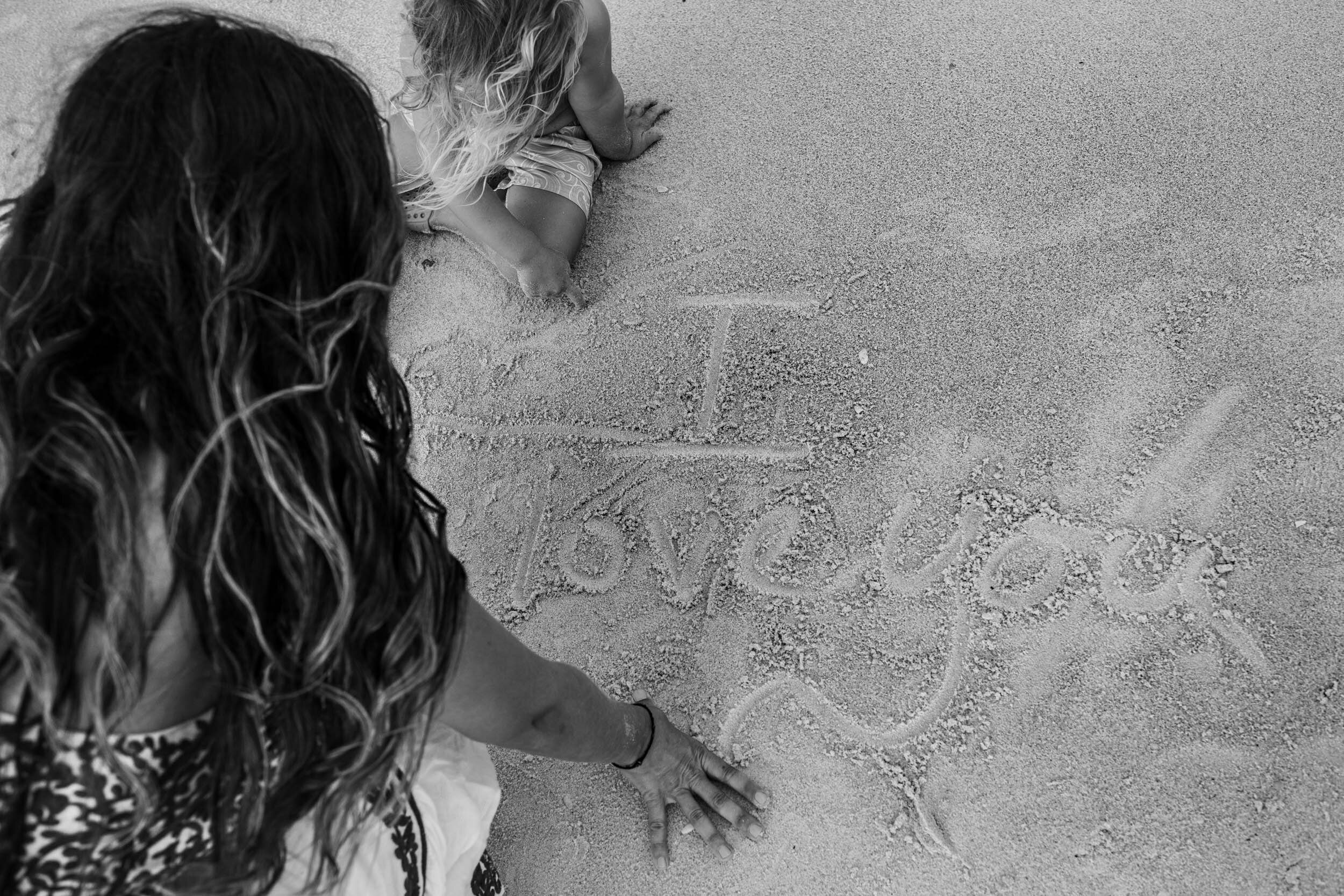 mom writing "I love you" in the sand at the beach