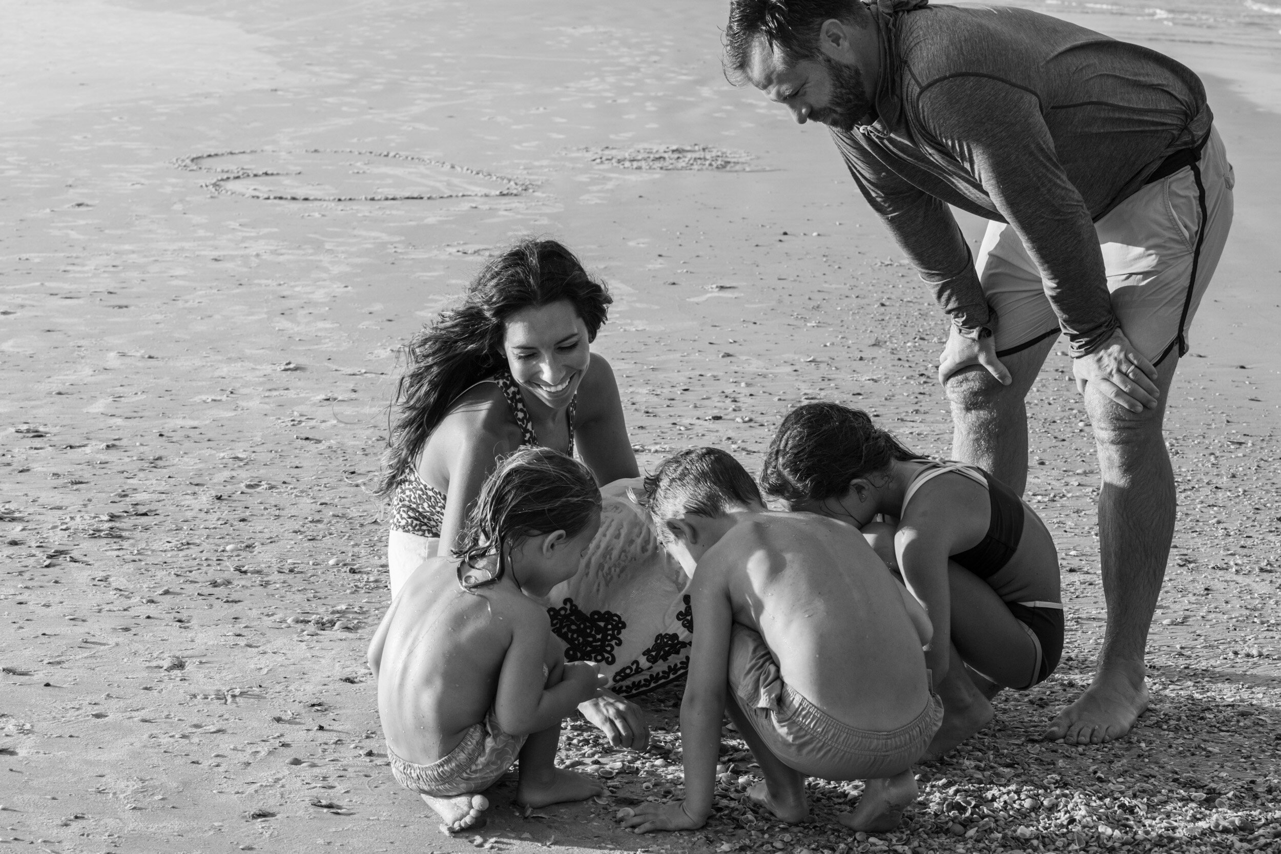 family playing in sand together at the beach