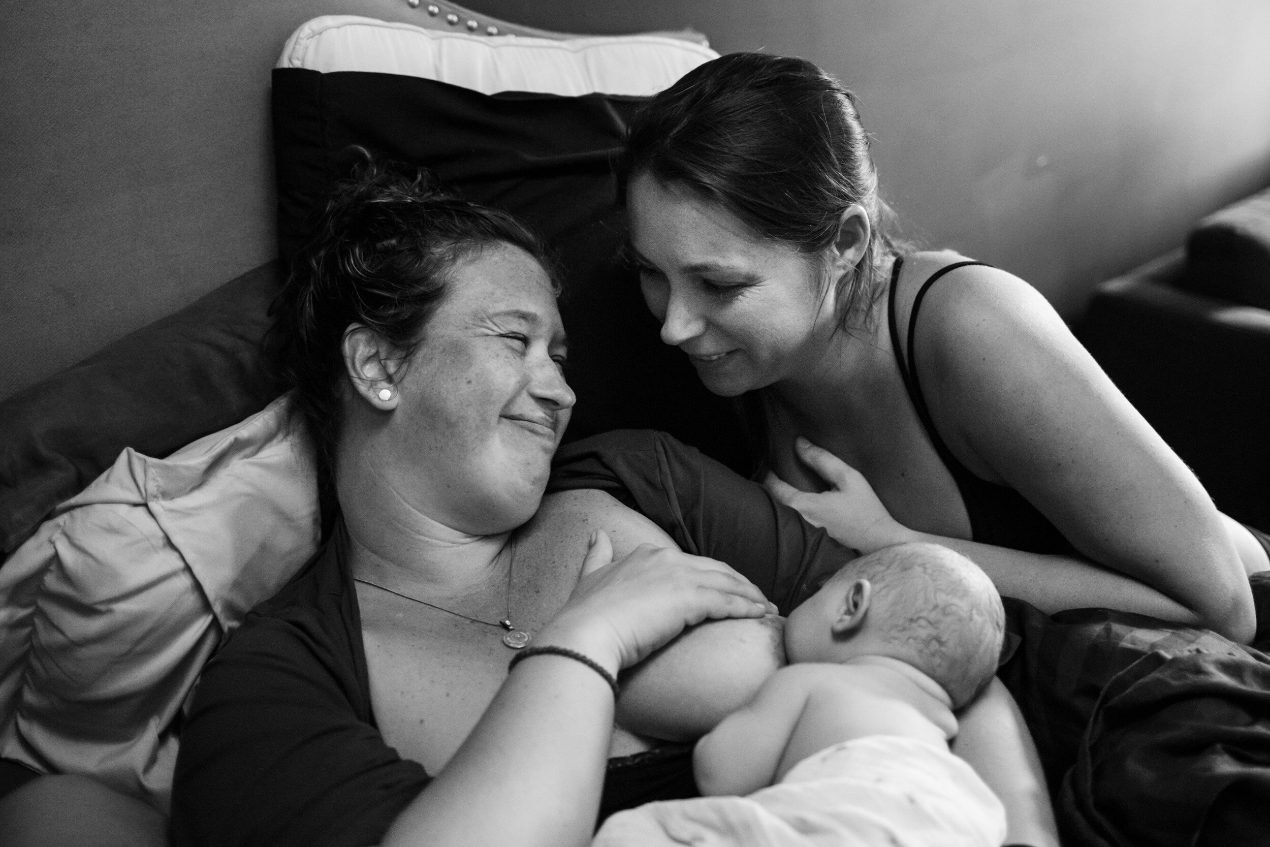 new parents smiling while holding their newborn baby as she breastfeeds
