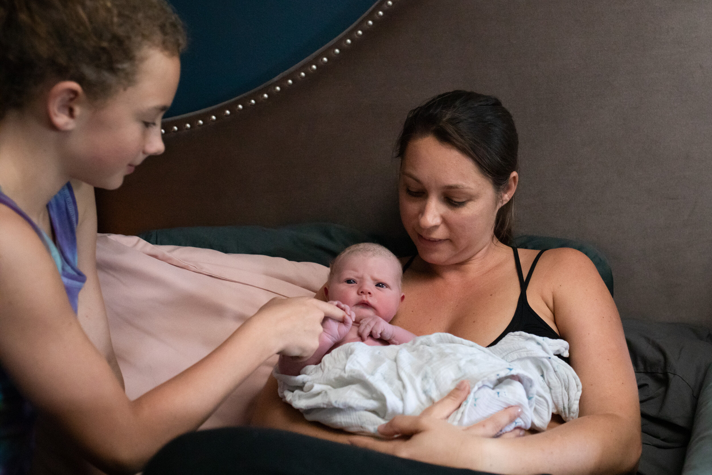 older sister holding hand of newborn baby sister