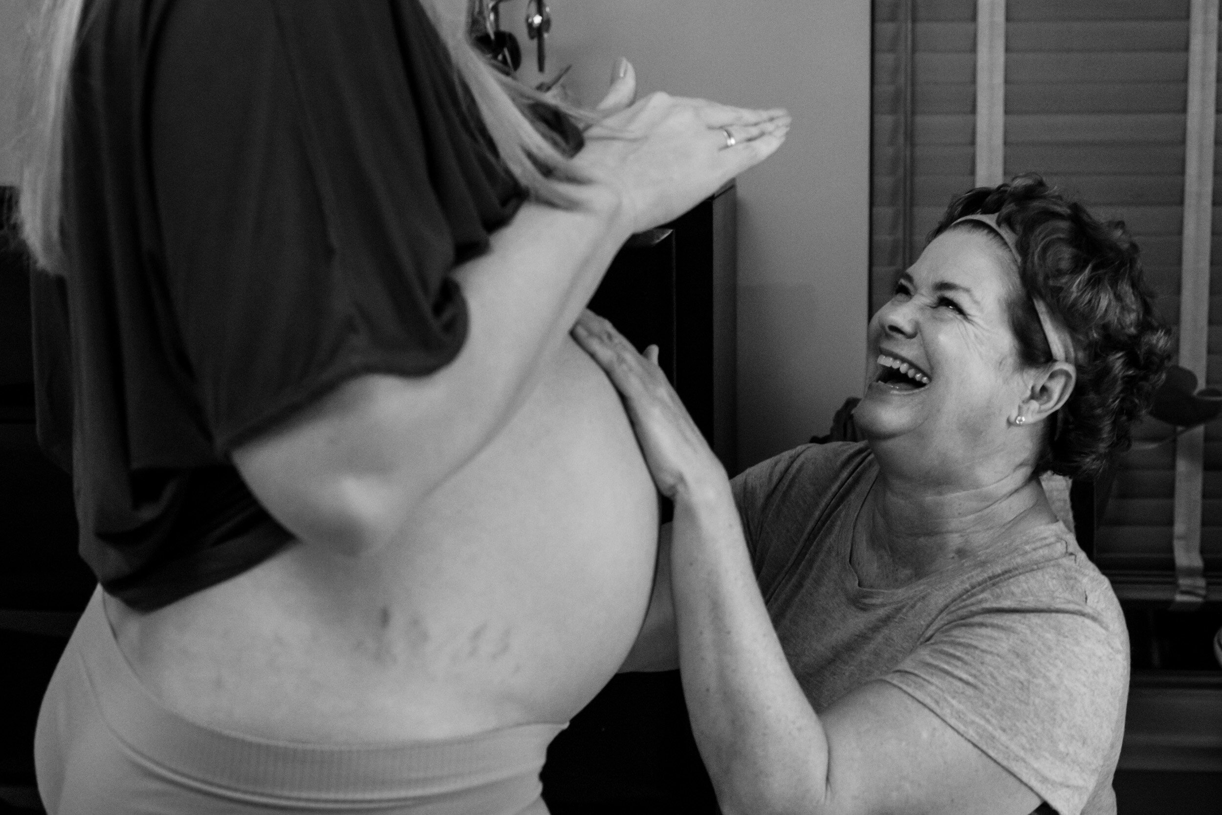 doula laughing at birth mom while palpating her belly