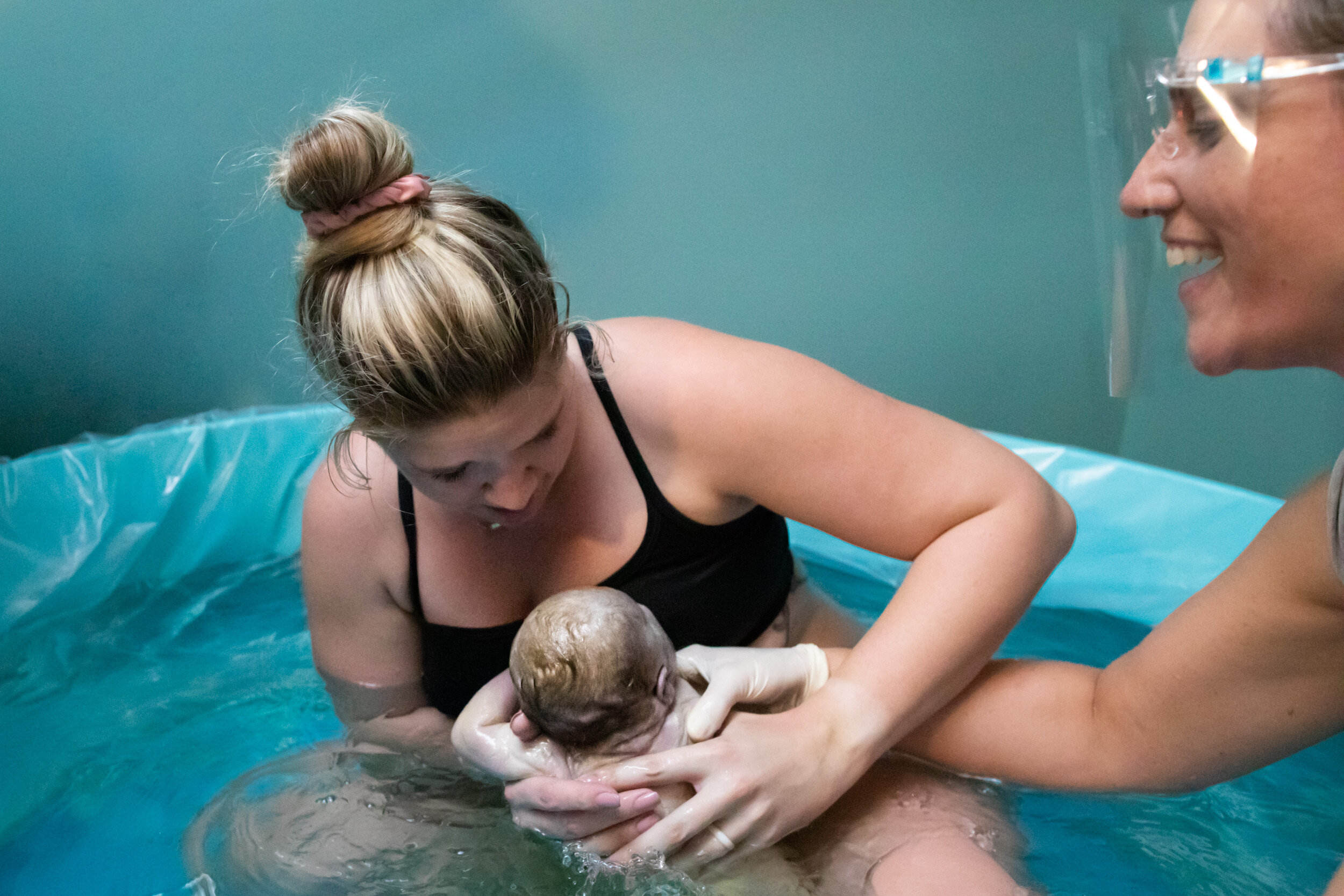birth mom pulling her baby out of the water in the birth pool with Midwife Christa of Transitions Jacksonville assisting