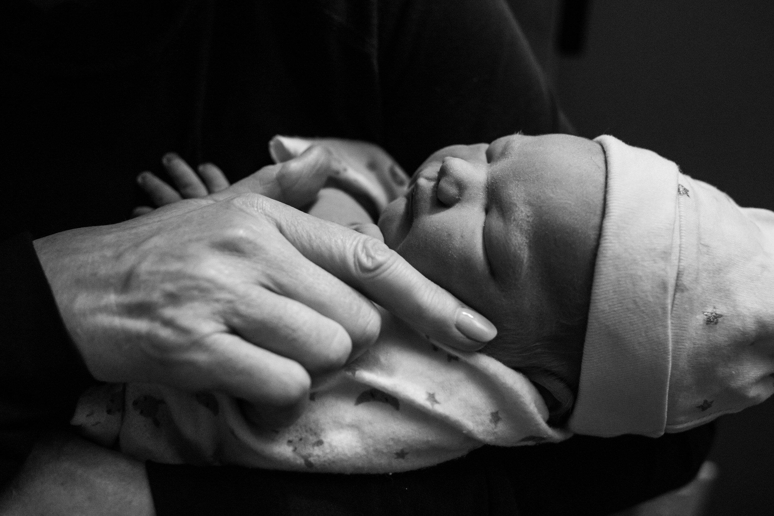 grandmother touching the face of her newborn granddaughter