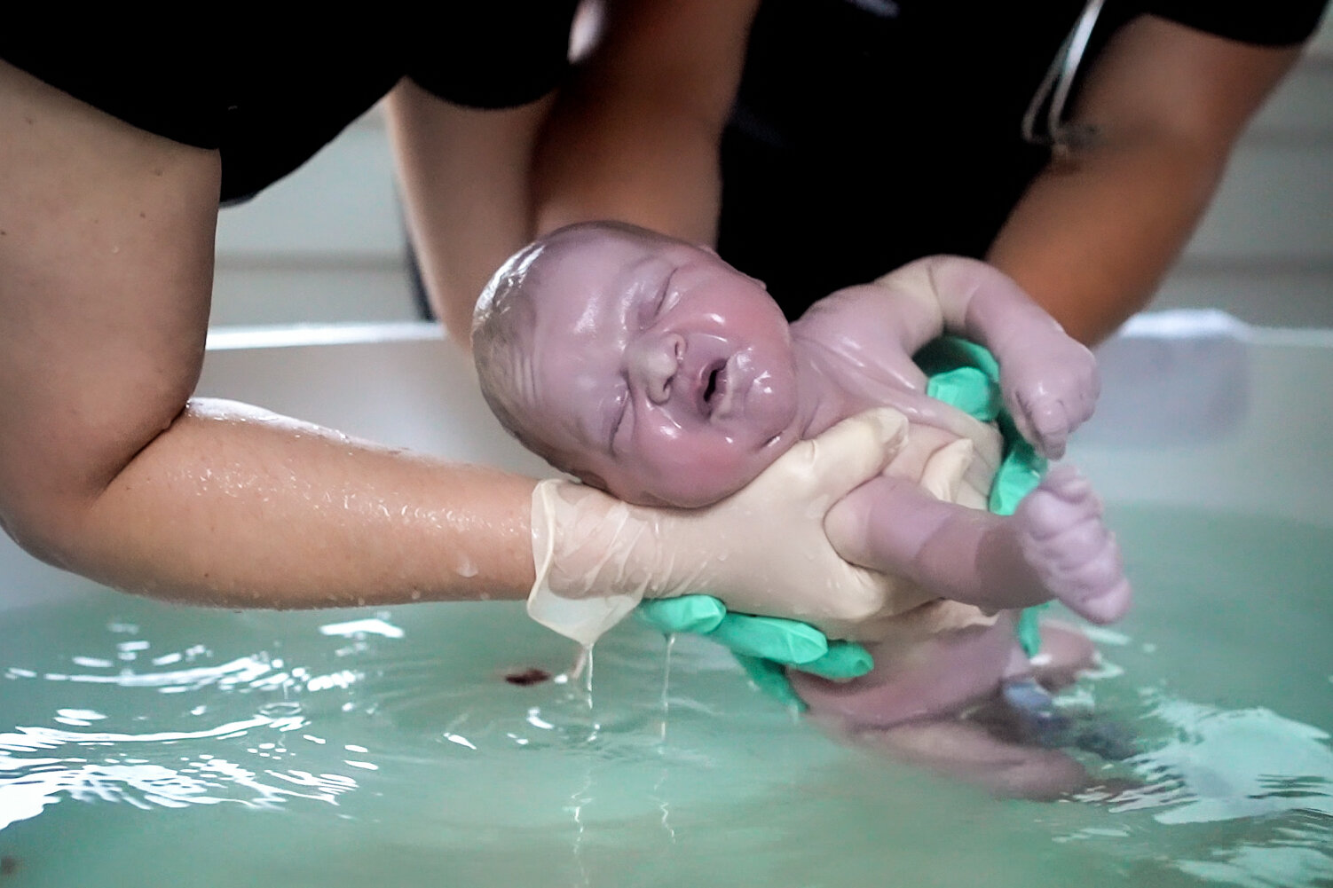 Newborn baby emerging from water in birth pool
