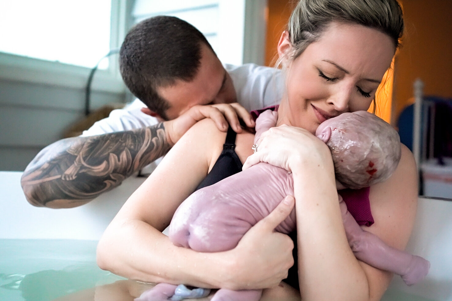 Mom holding her baby just after birth, while her husband tears up