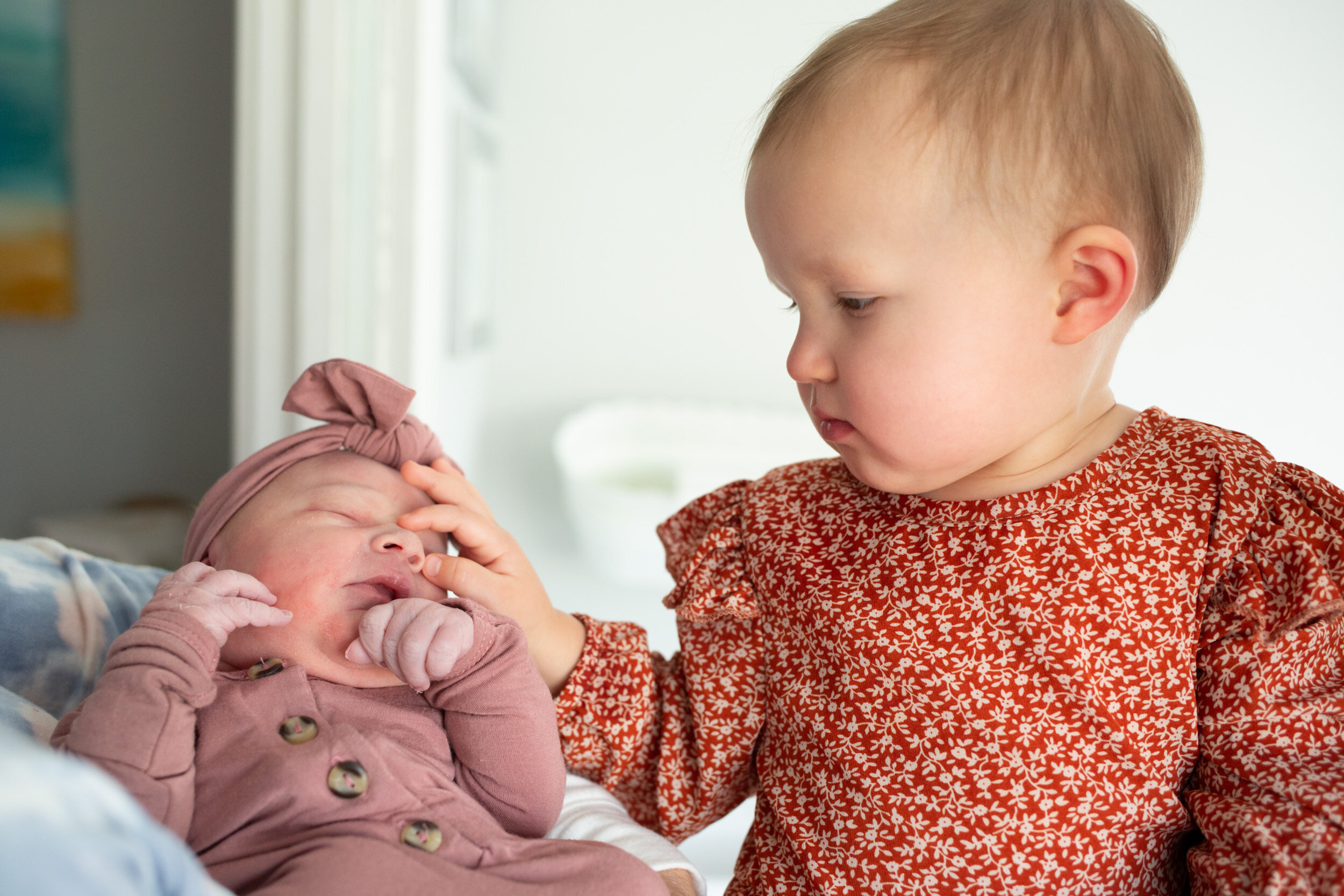 Older sister touching the nose of her newborn baby sister