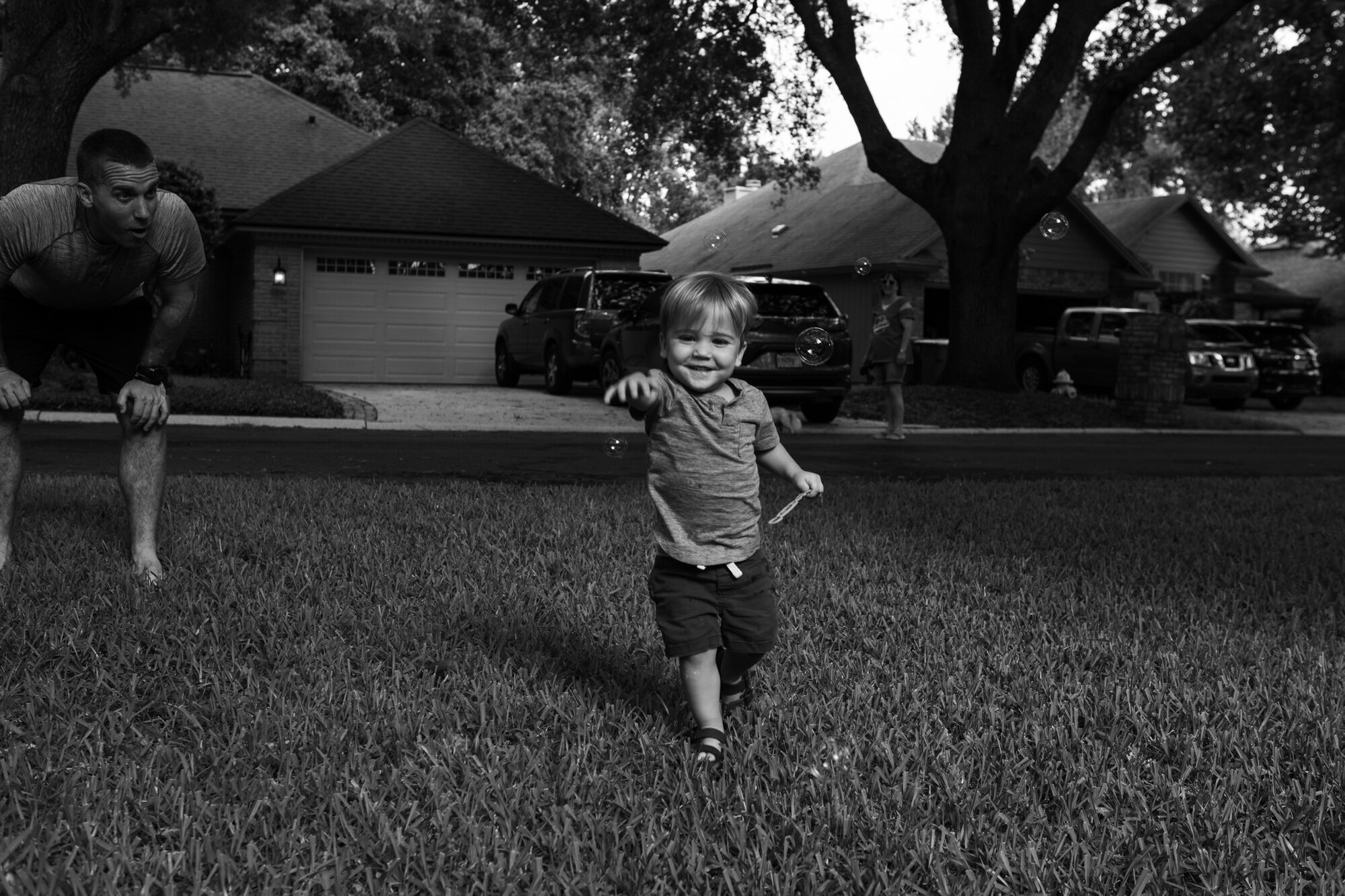 little boy chasing bubbles while dad watches and cheers him on