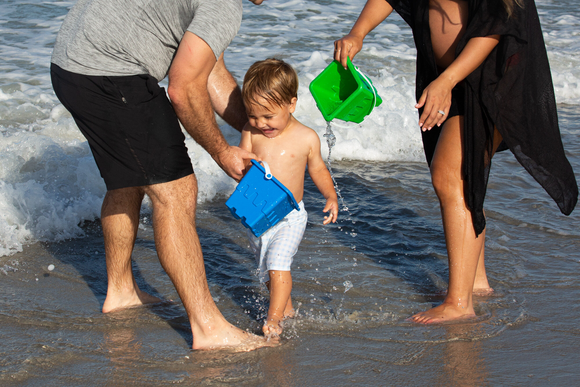 parents dumping water buckets on their little boy as he laughs