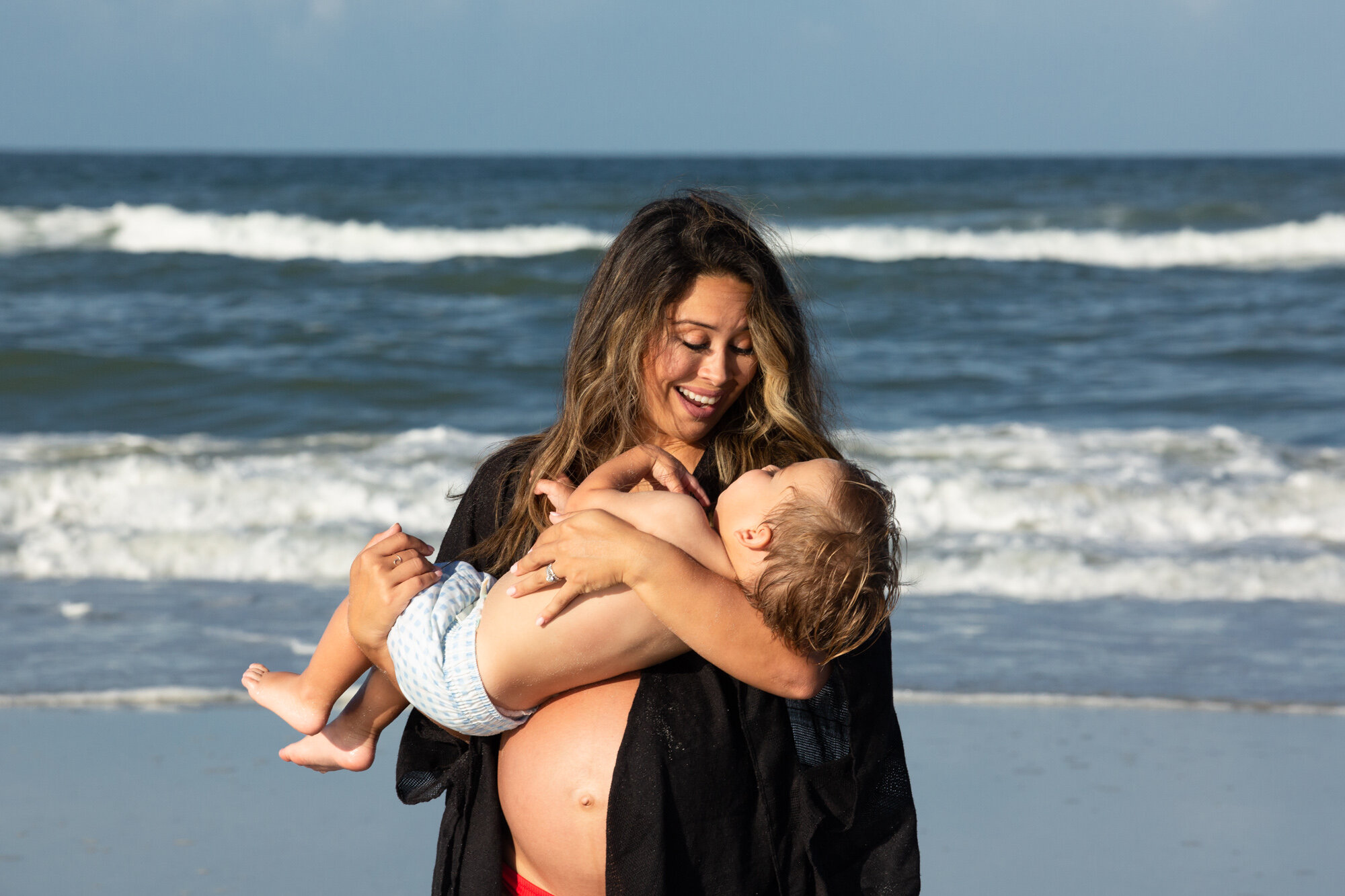pregnant mom holding her little boy on the beach