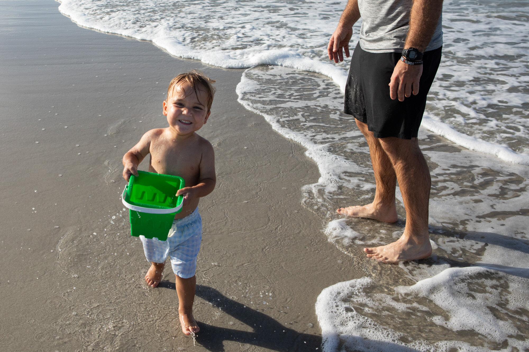 little boy running and laughing with a bucket of water