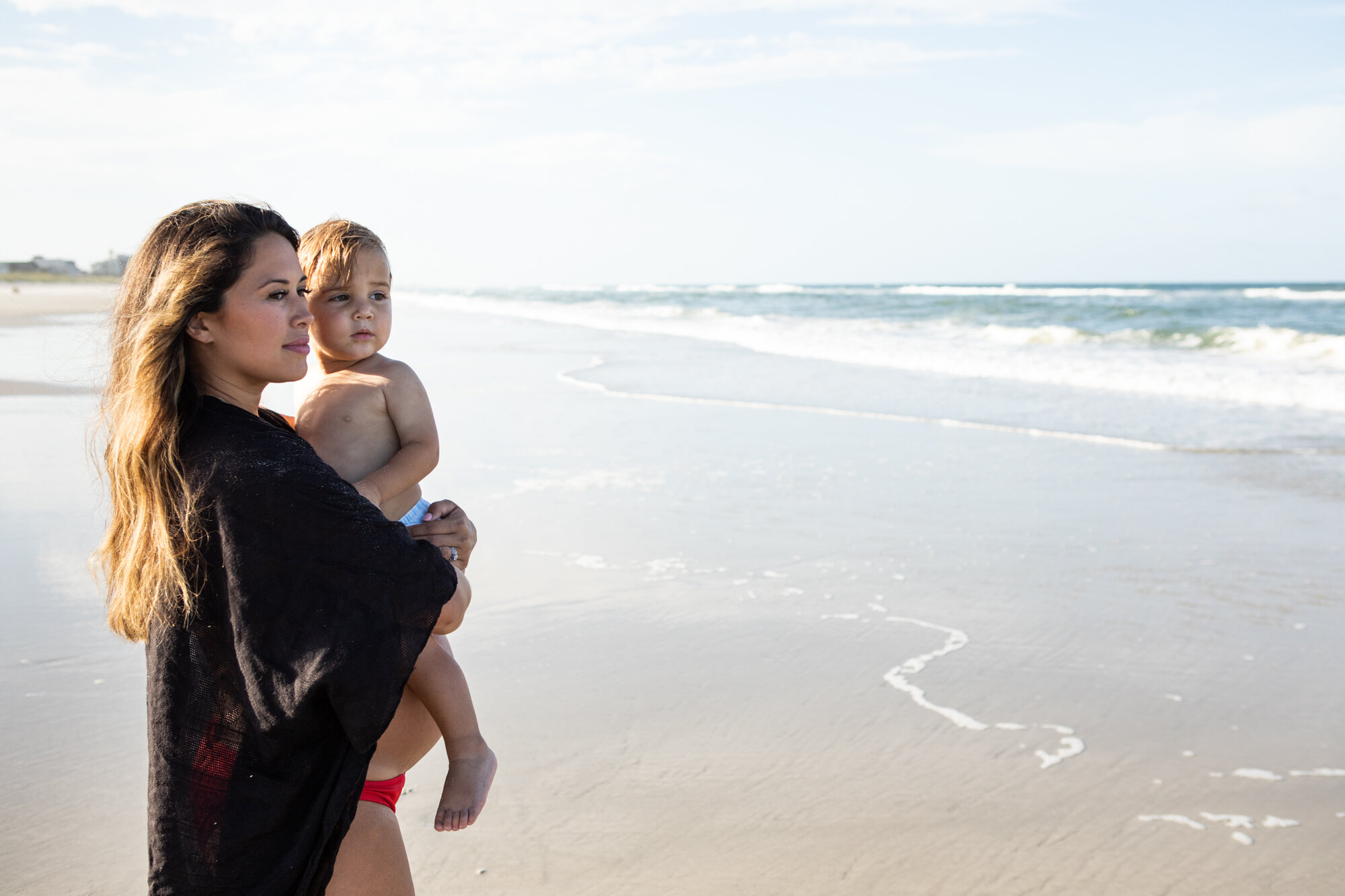 pregnant mom holding her little boy while looking at the ocean