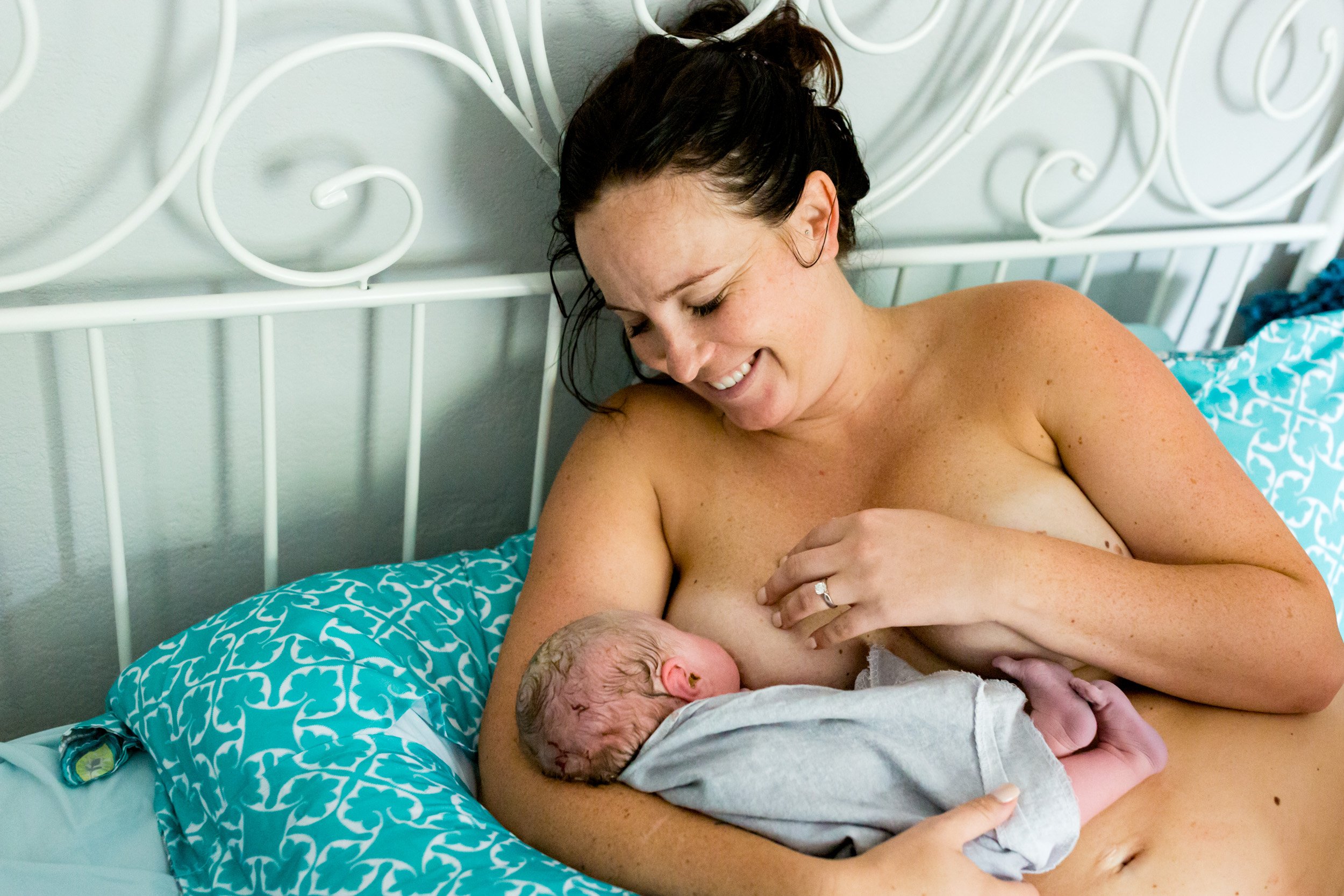 new mom smiling at her newborn baby as she latches for the first time