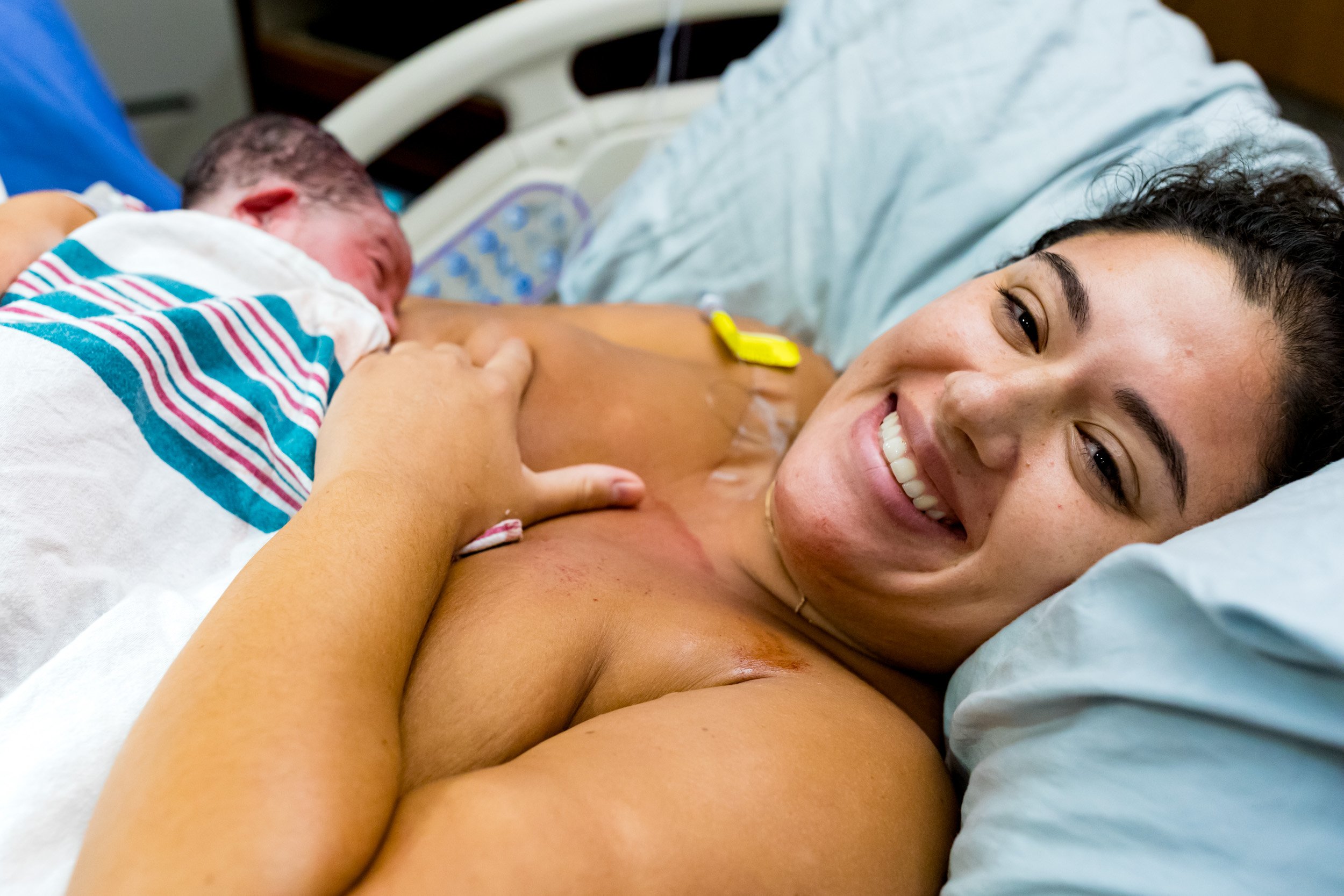 birth mom smiling at me after birth, while nursing her newborn