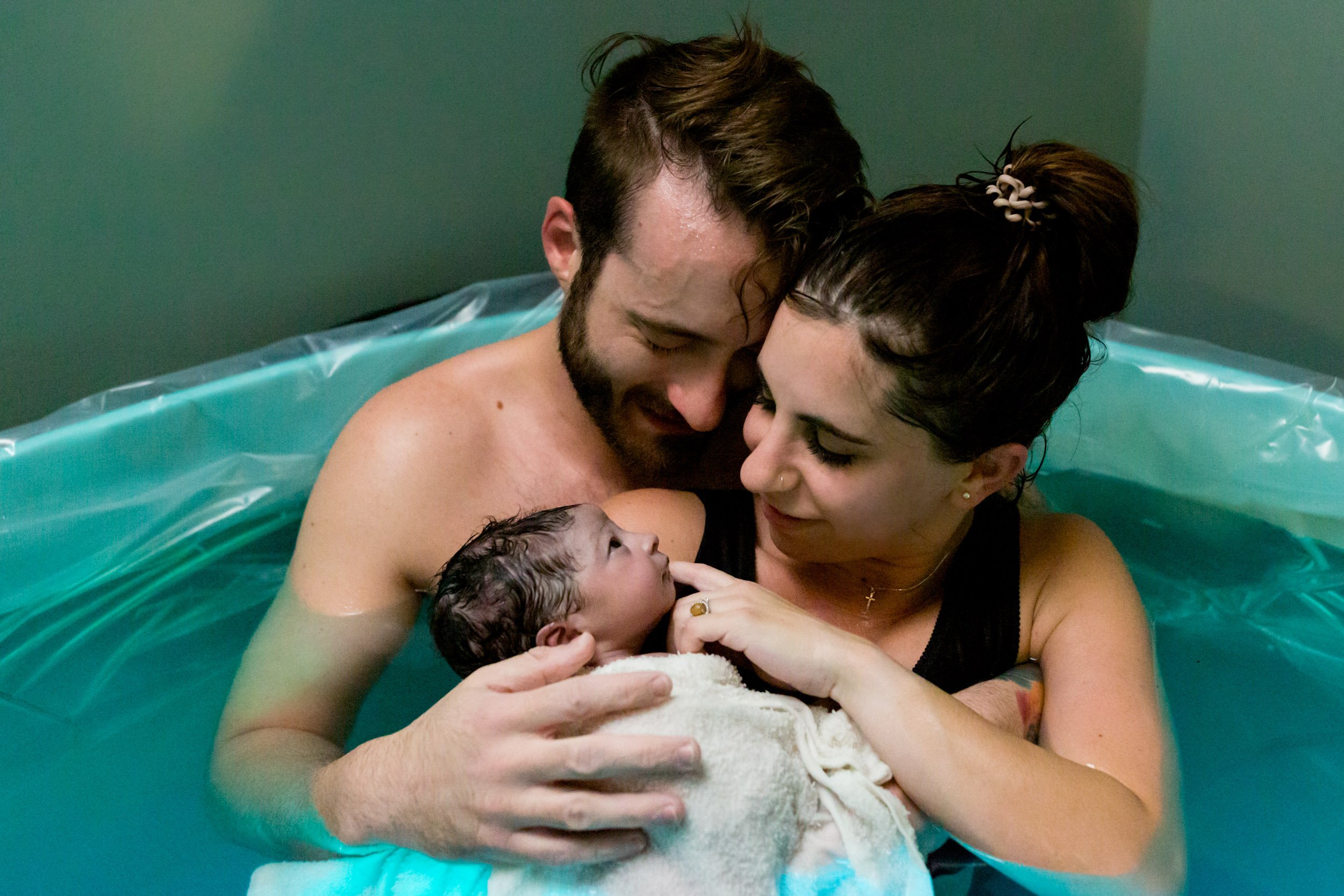 new parents smiling and holding their baby girl in the birth tub - transitions birth center