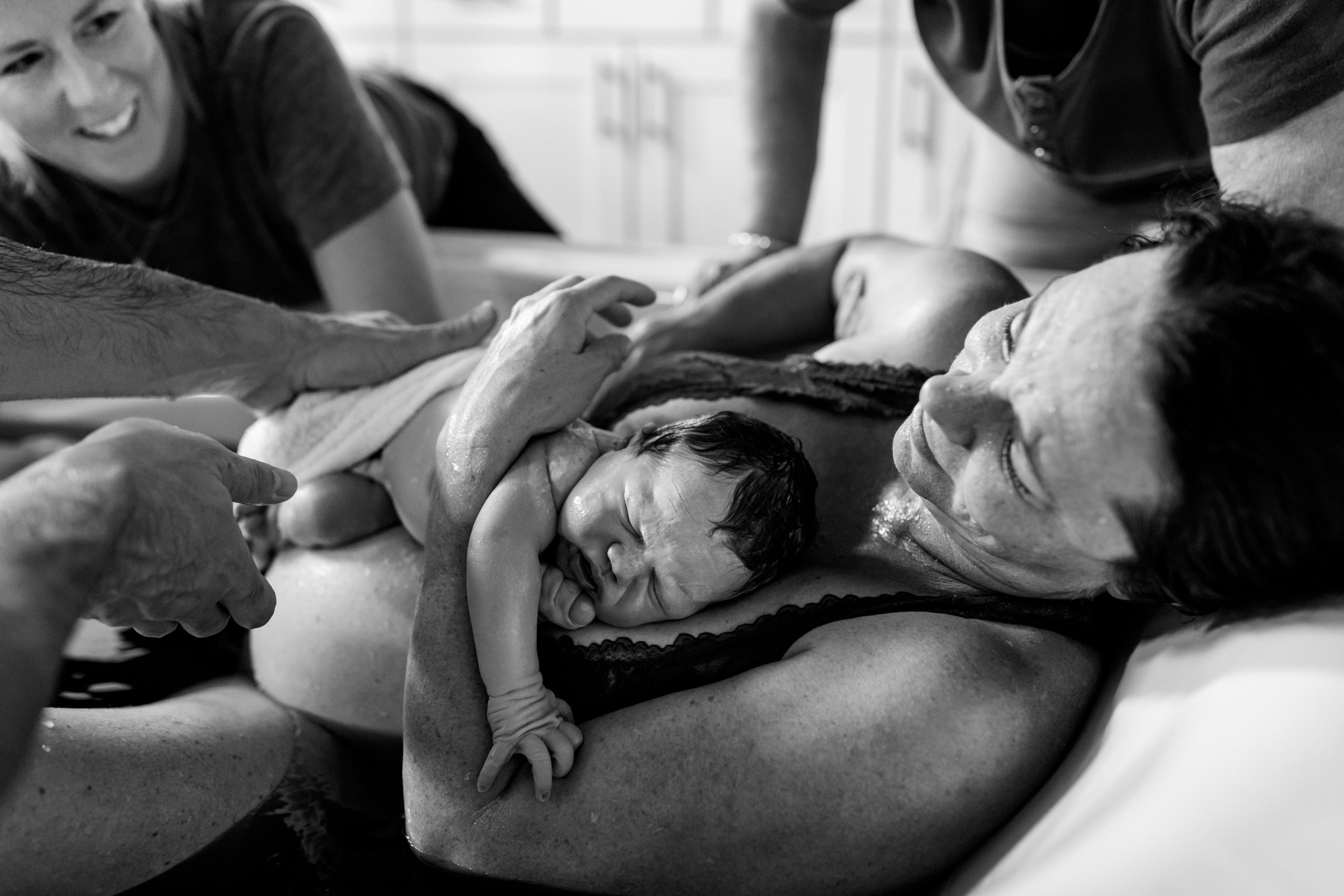 born into water, newborn baby rests on her mom's chest and the midwife gets ready to receive the placenta