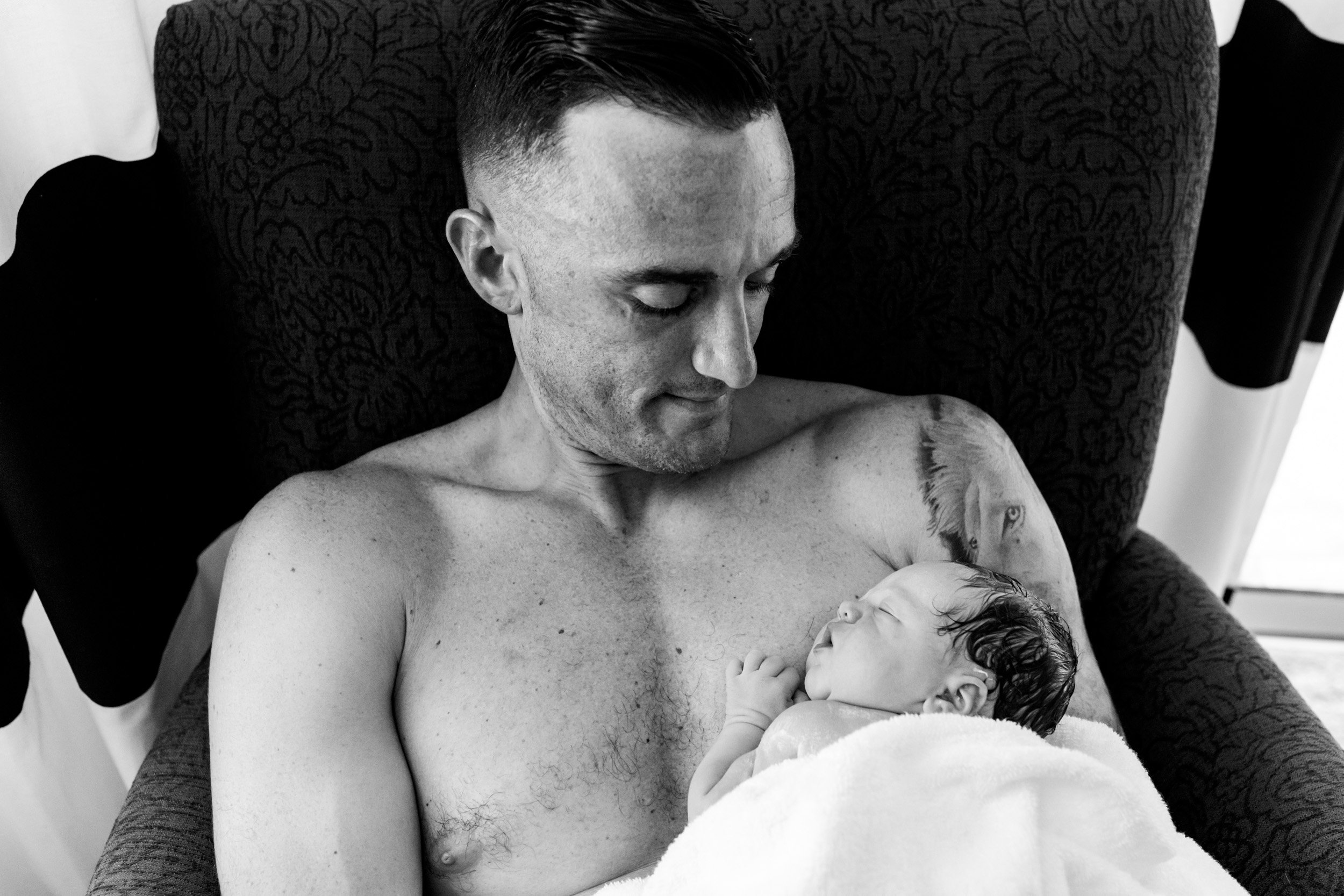 dad holding his newborn baby on his chest and looking down at her