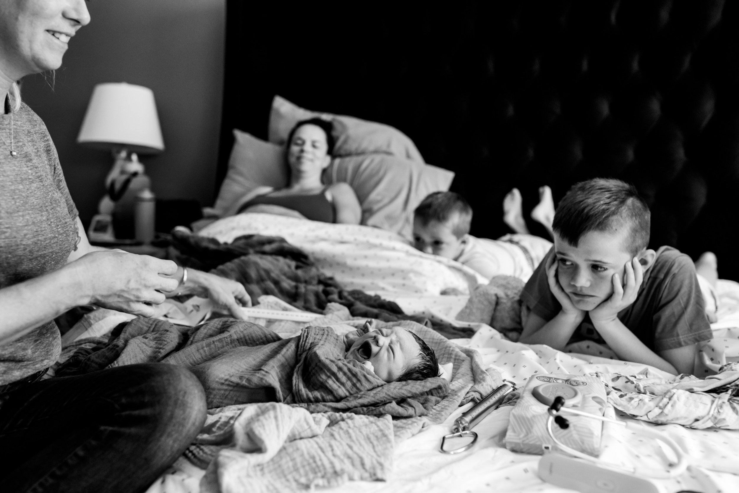 older brothers watch as the midwife performs the newborn exam