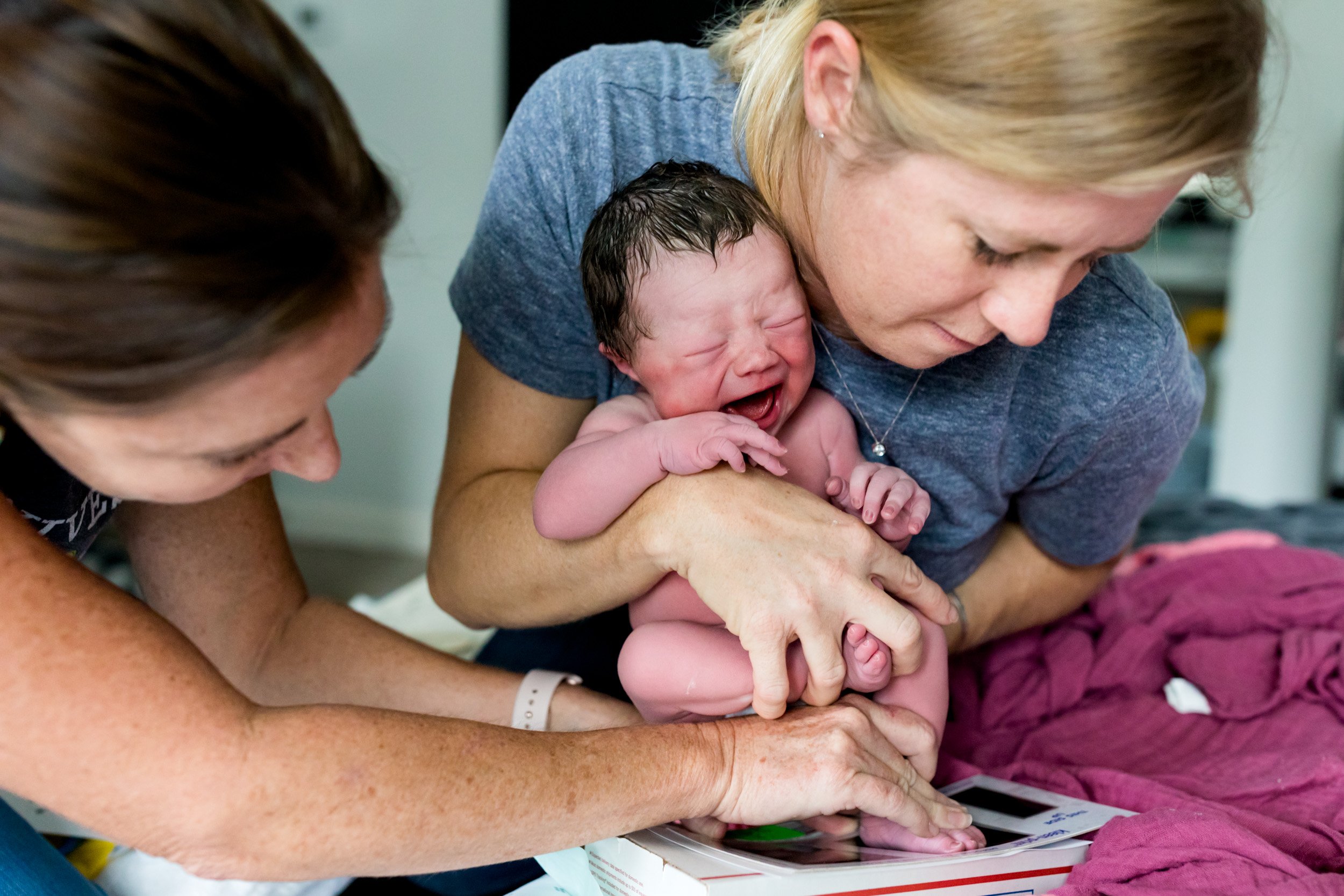 midwife holding baby and making footprints with her assistant helping