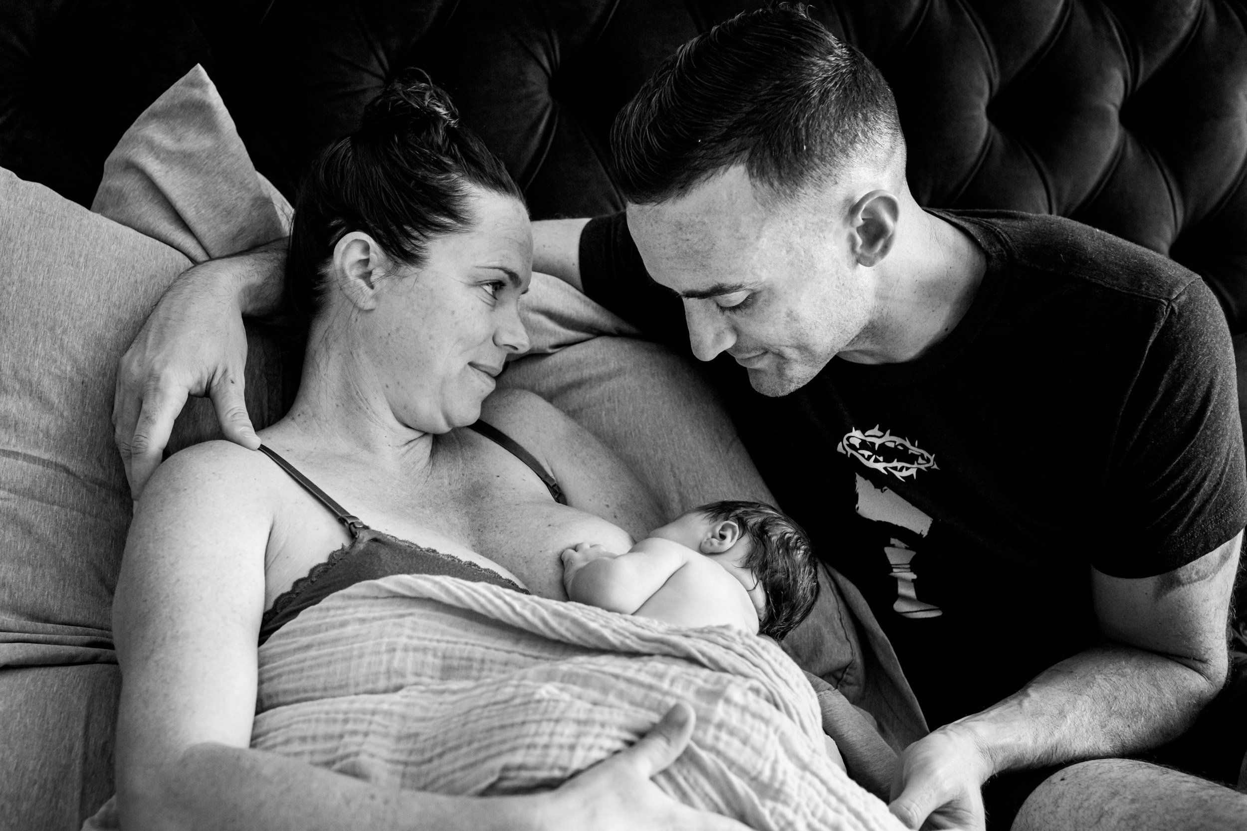 wife looking at her husband lovingly while he looks at their newborn baby girl just after birth