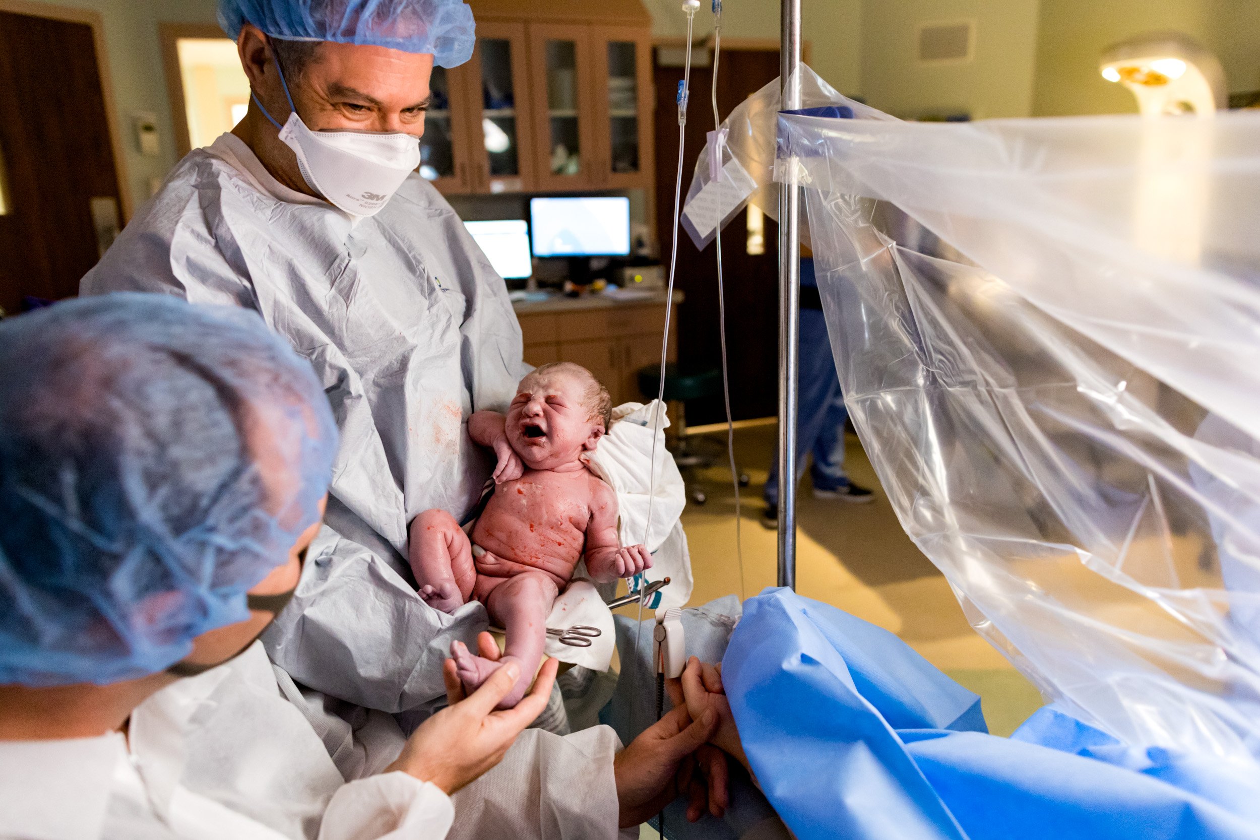 pediatrician holding baby for the parents to see just after birth in the OR