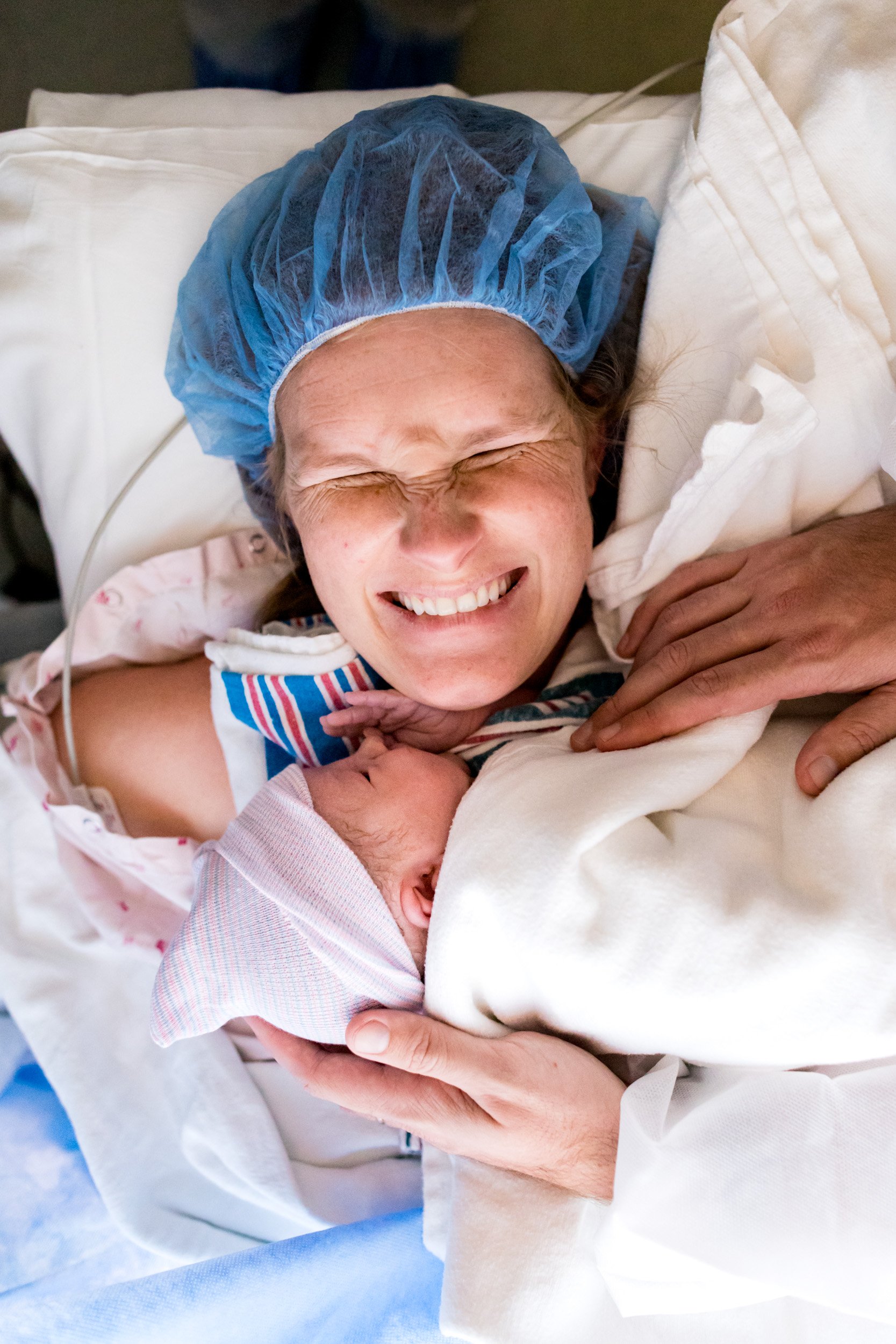 mom laughing with excitement while holding her newborn baby in the OR