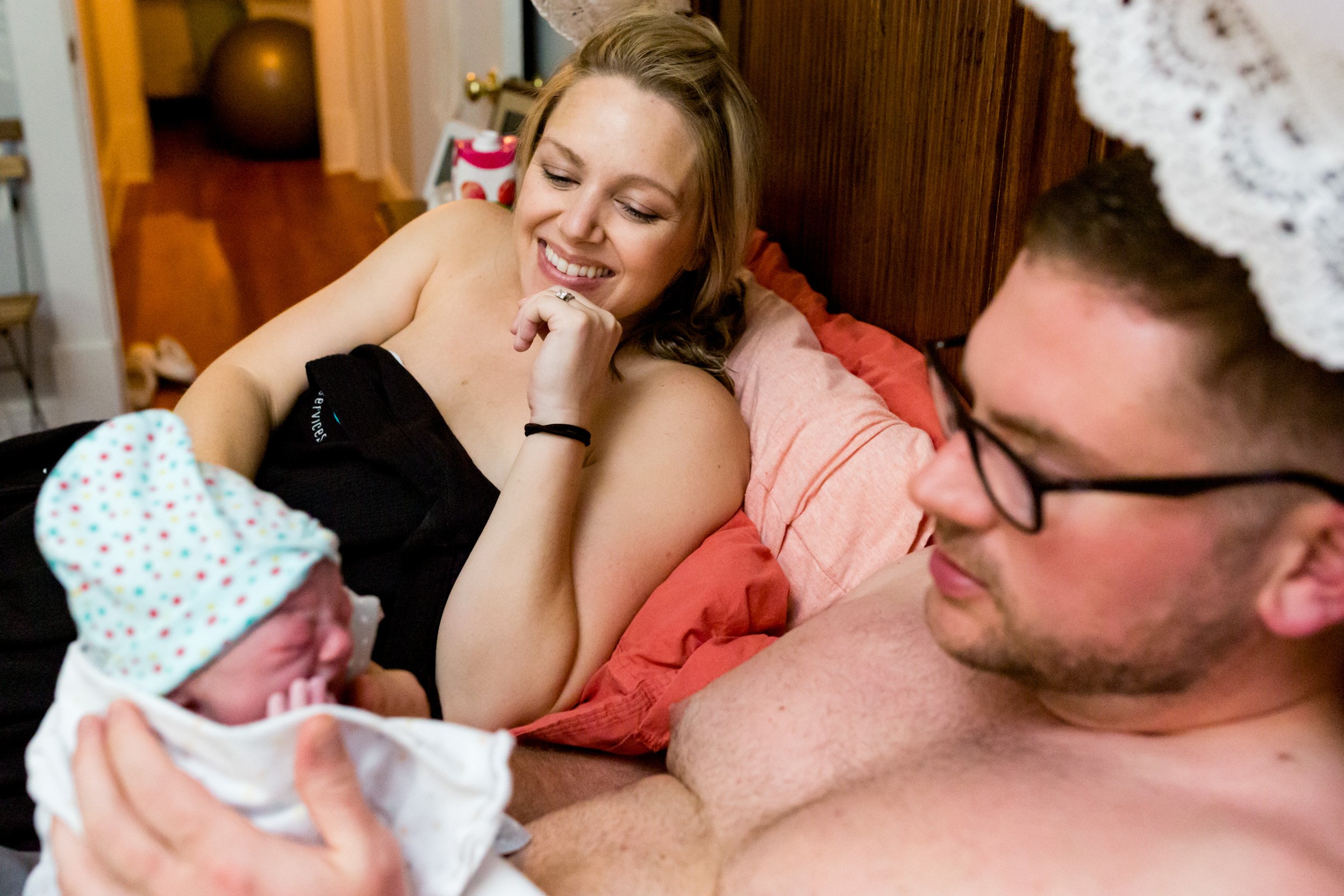 birth mom smiling at her husband as he holds their newborn baby girl