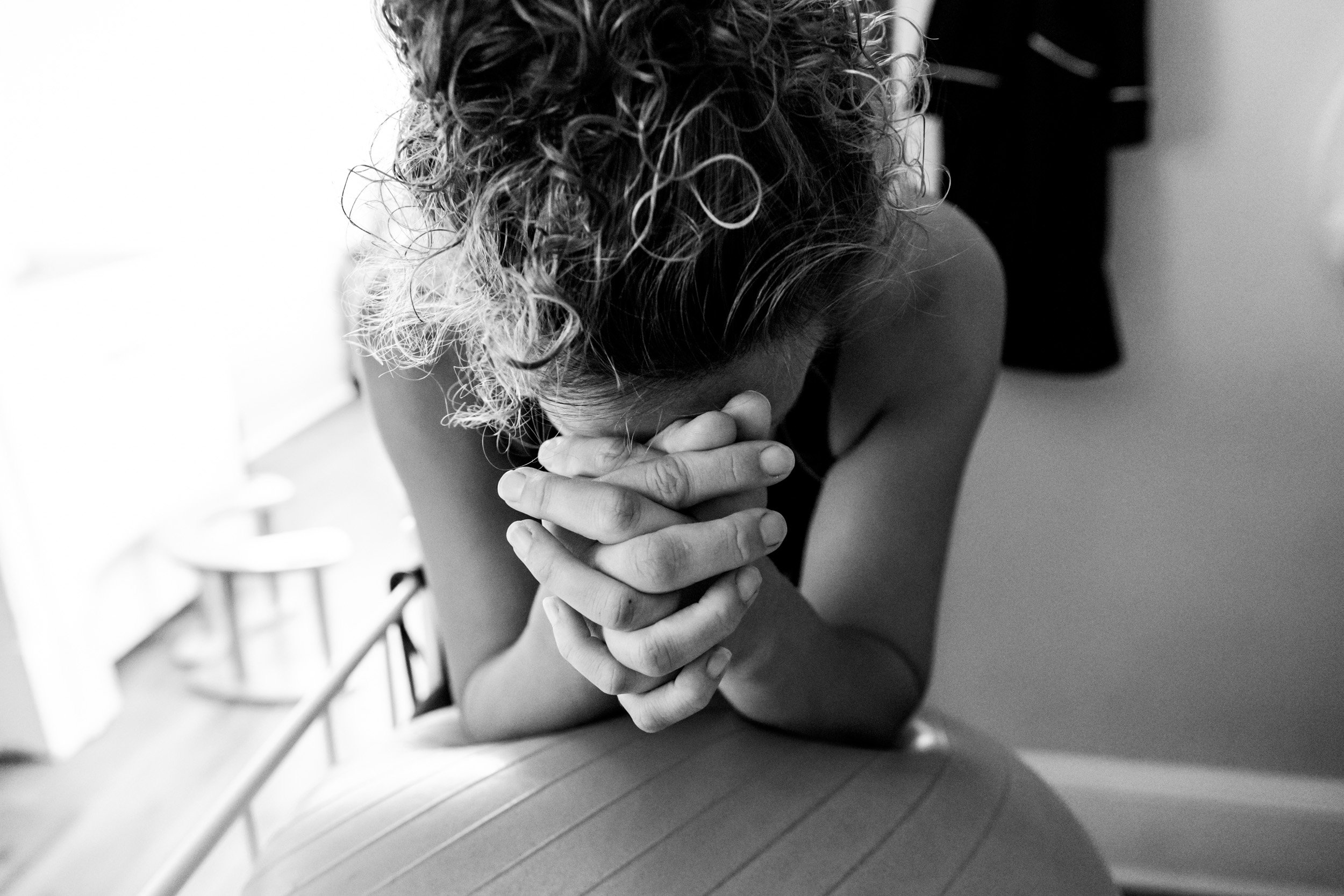 birth mom leaning over birth ball with her hands folded, while having a contraction