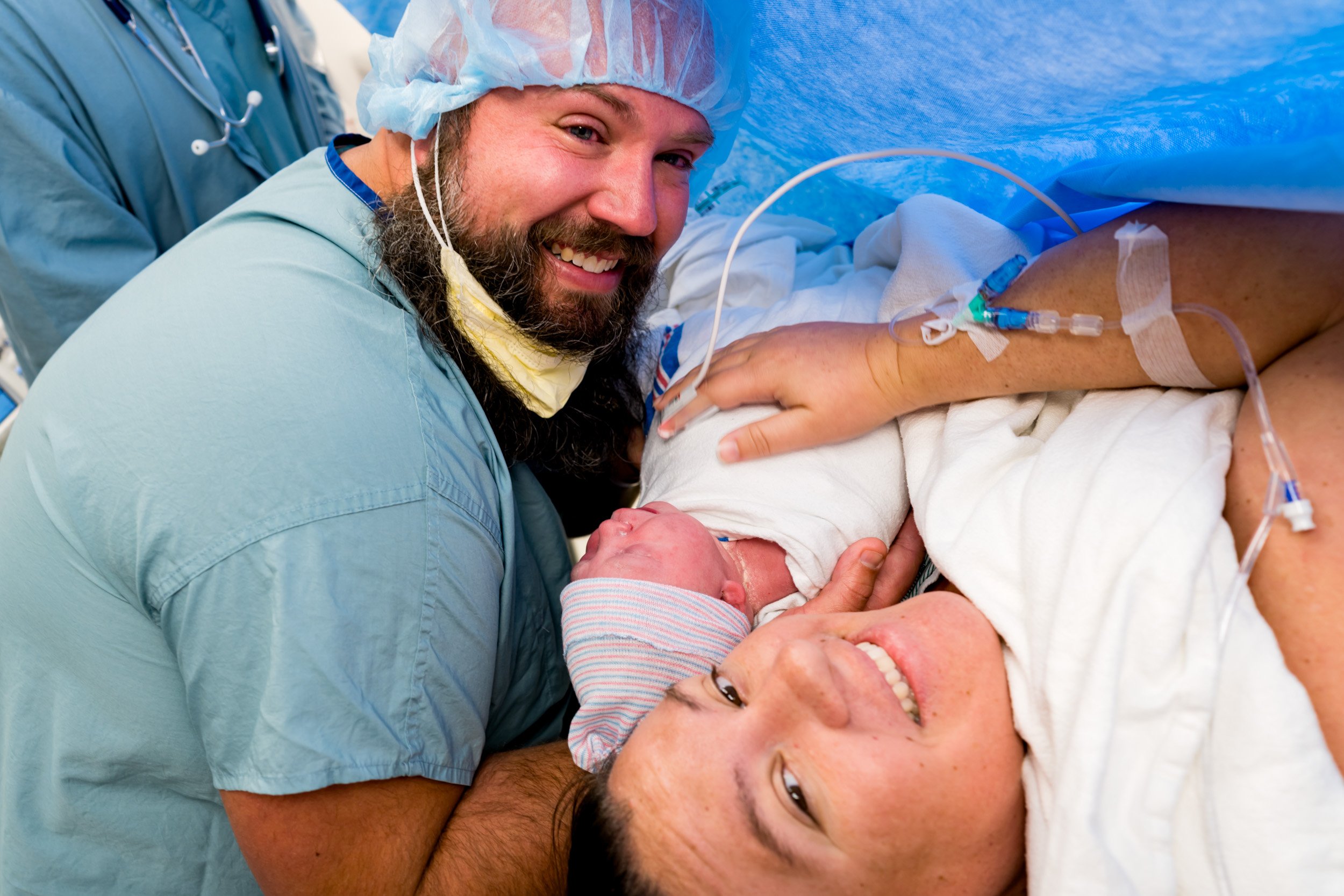 dad and mom smiling at the camera while holding newborn baby