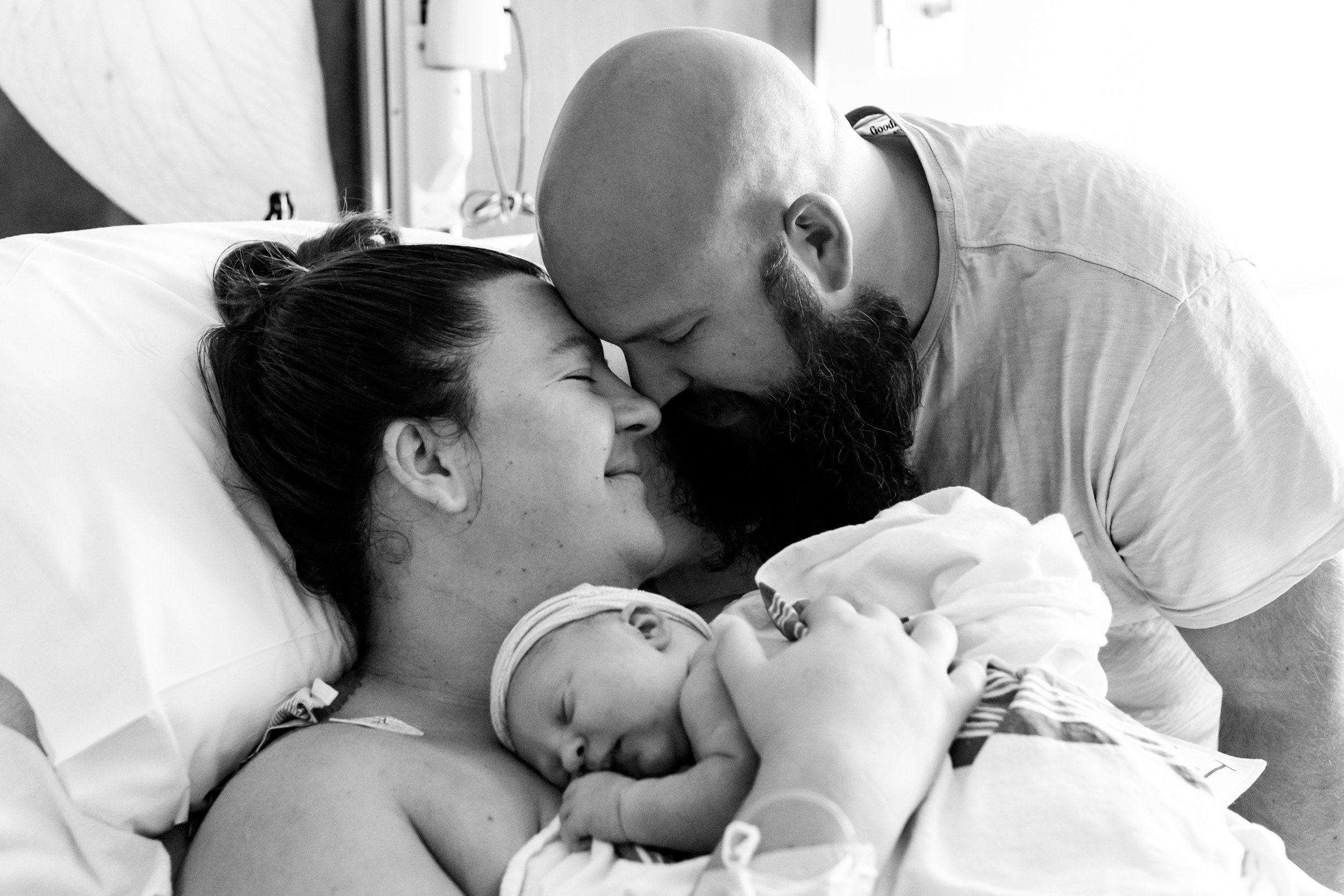 new parents with their heads together holding their baby girl just after birth