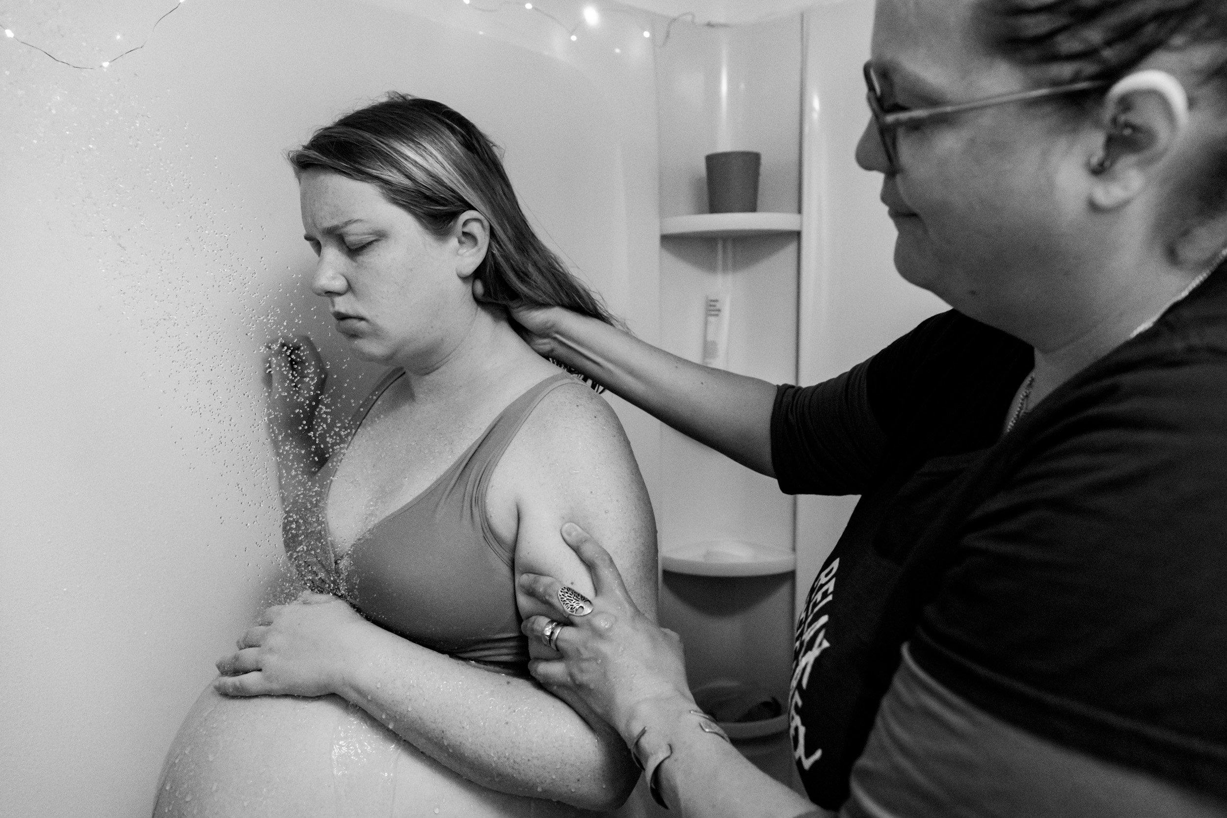 doula massaging laboring mom's neck while she showers