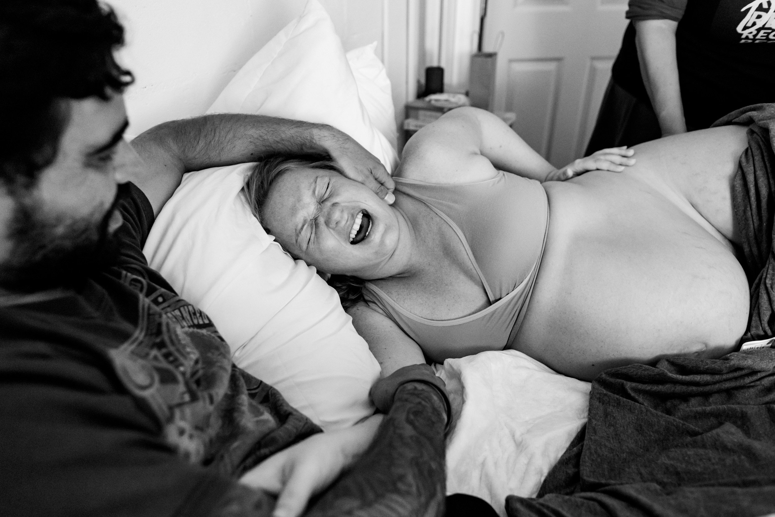 birth mom wincing in pain as her husband holds her during a contraction