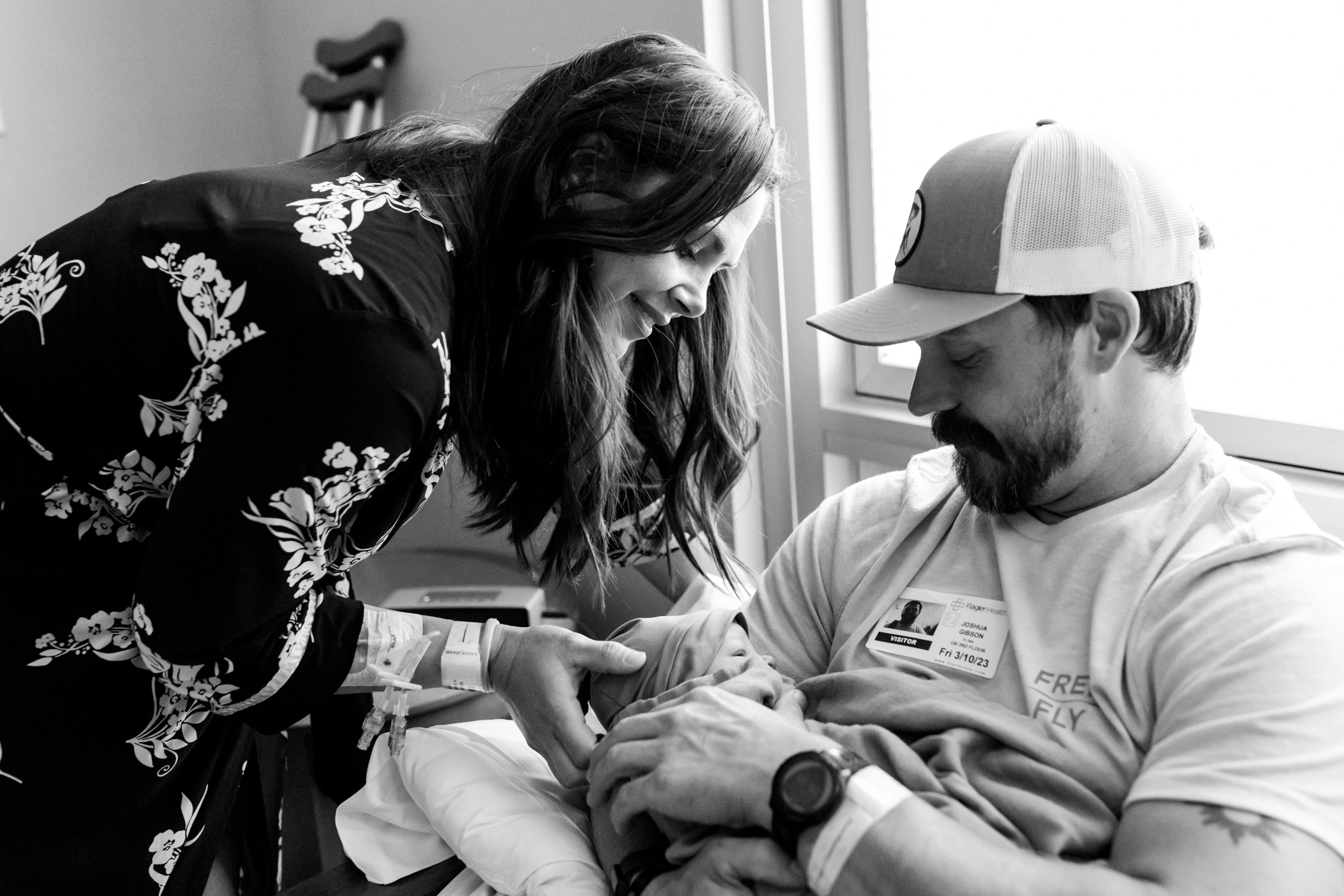 birth mom looking at her newborn baby boy as her husband holds him