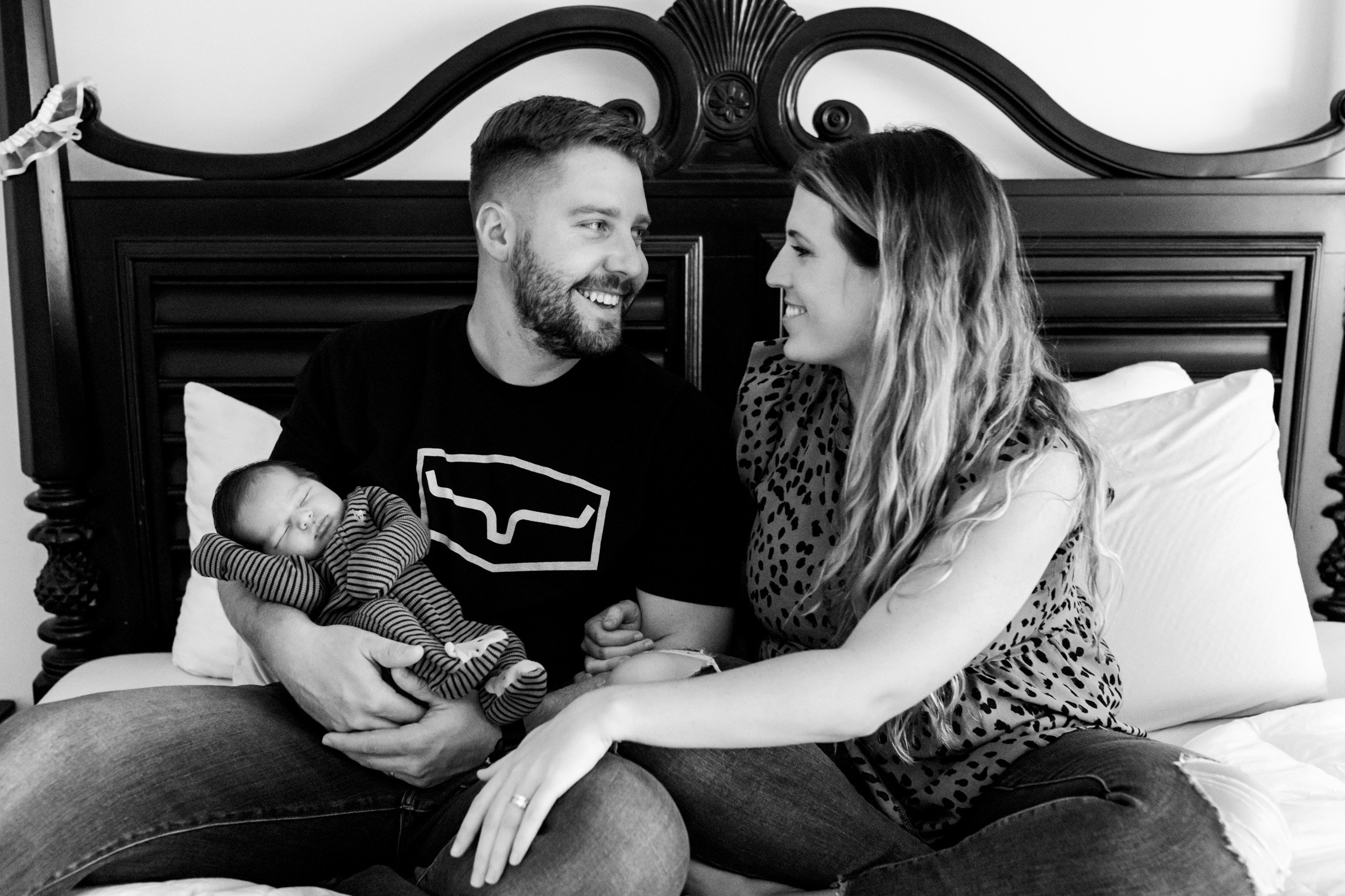 mom and dad looking at each other and smiling while holding their newborn baby