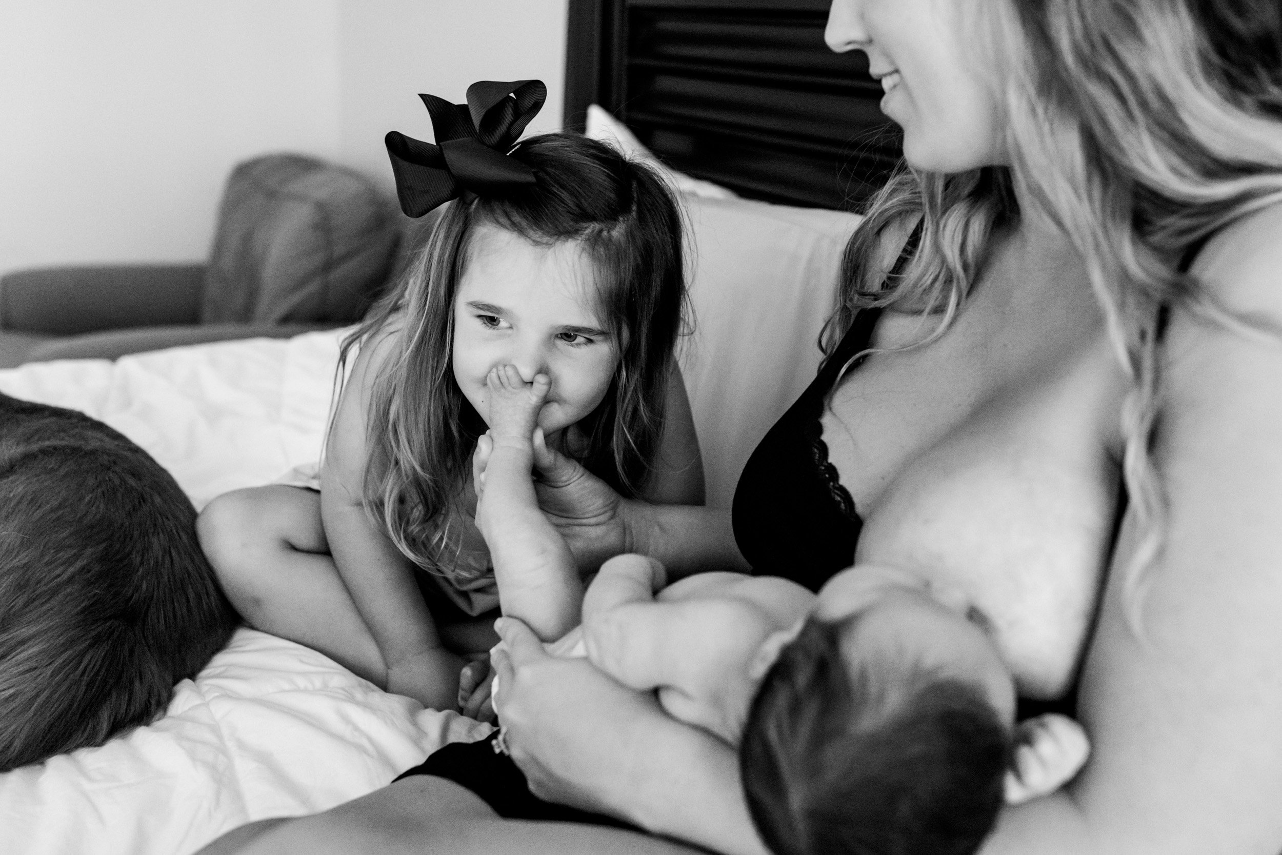 little girl smelling newborn baby's feet